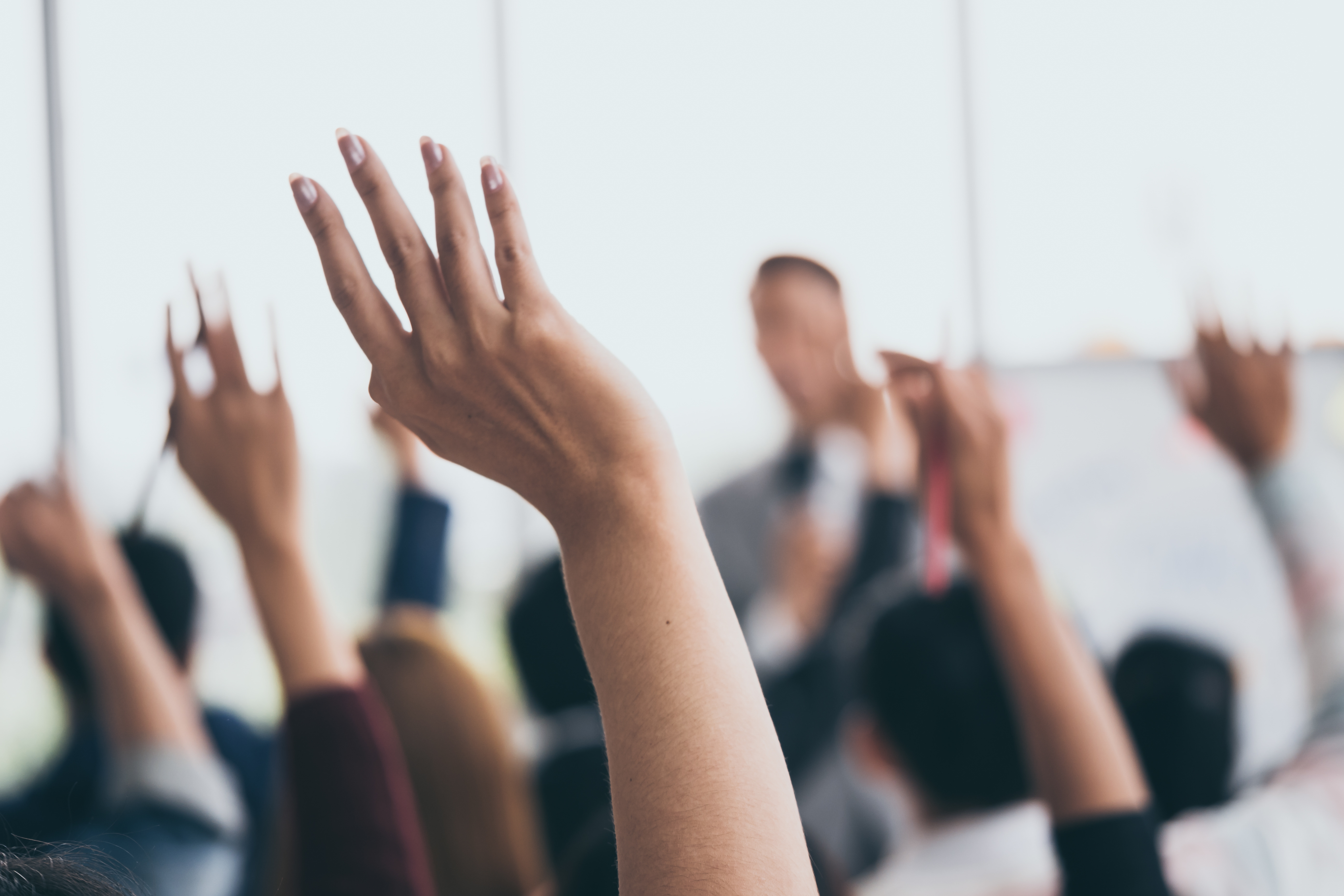 Audience raising hands up while businessman is speaking in training at the office.