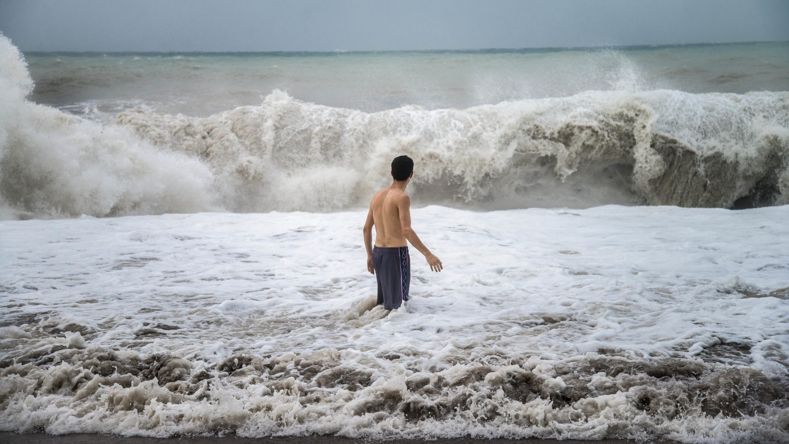 Antalya - Turkey - October 17, 2013: Young man standing against the sea waves with splash in a cloudy storm weather