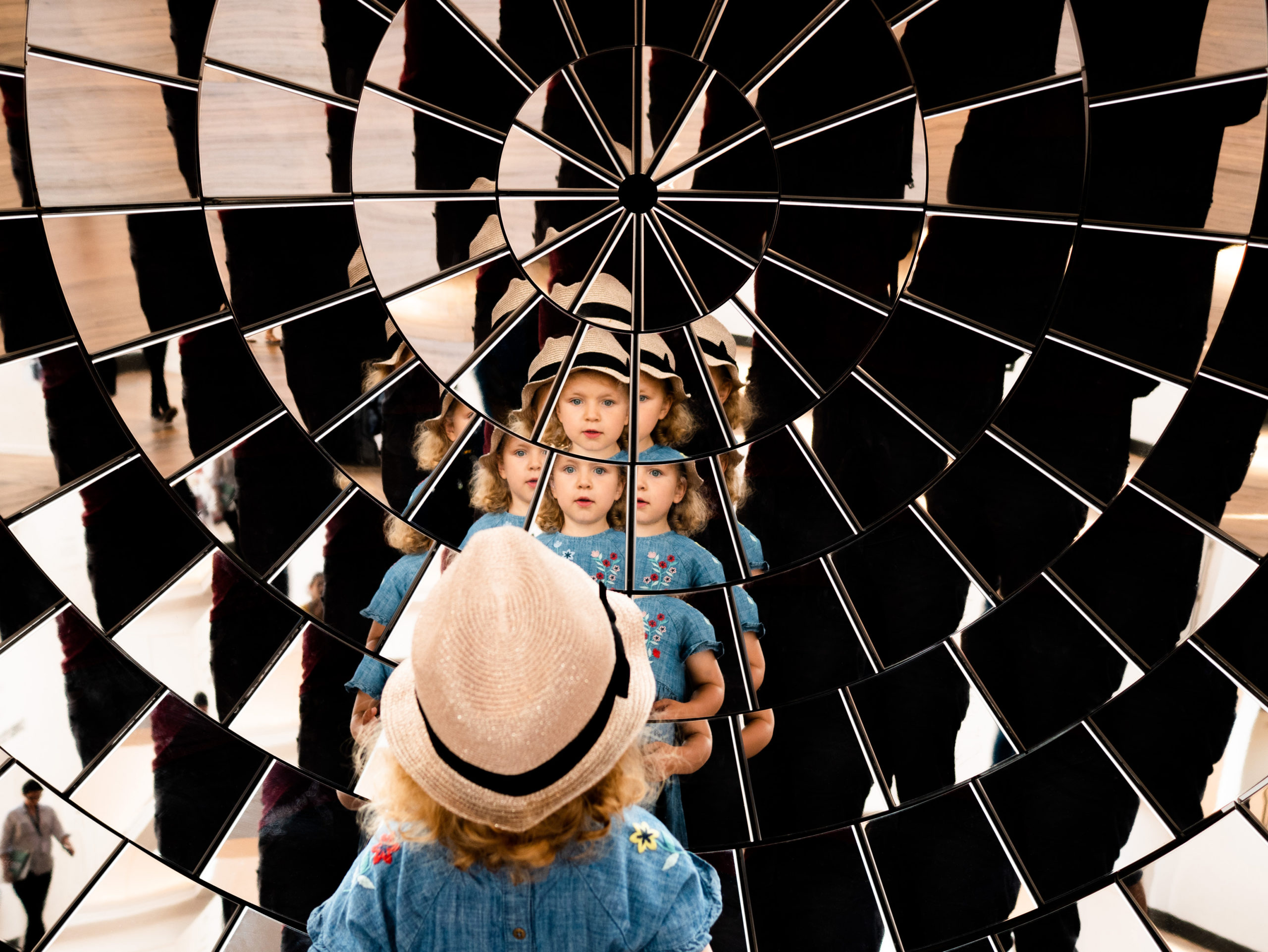 Girl's reflection in many mirrors arranged in a parabolic shape. Multiple points of view, multiple angles. Fragmented multi-faceted portrait. Mirror array.