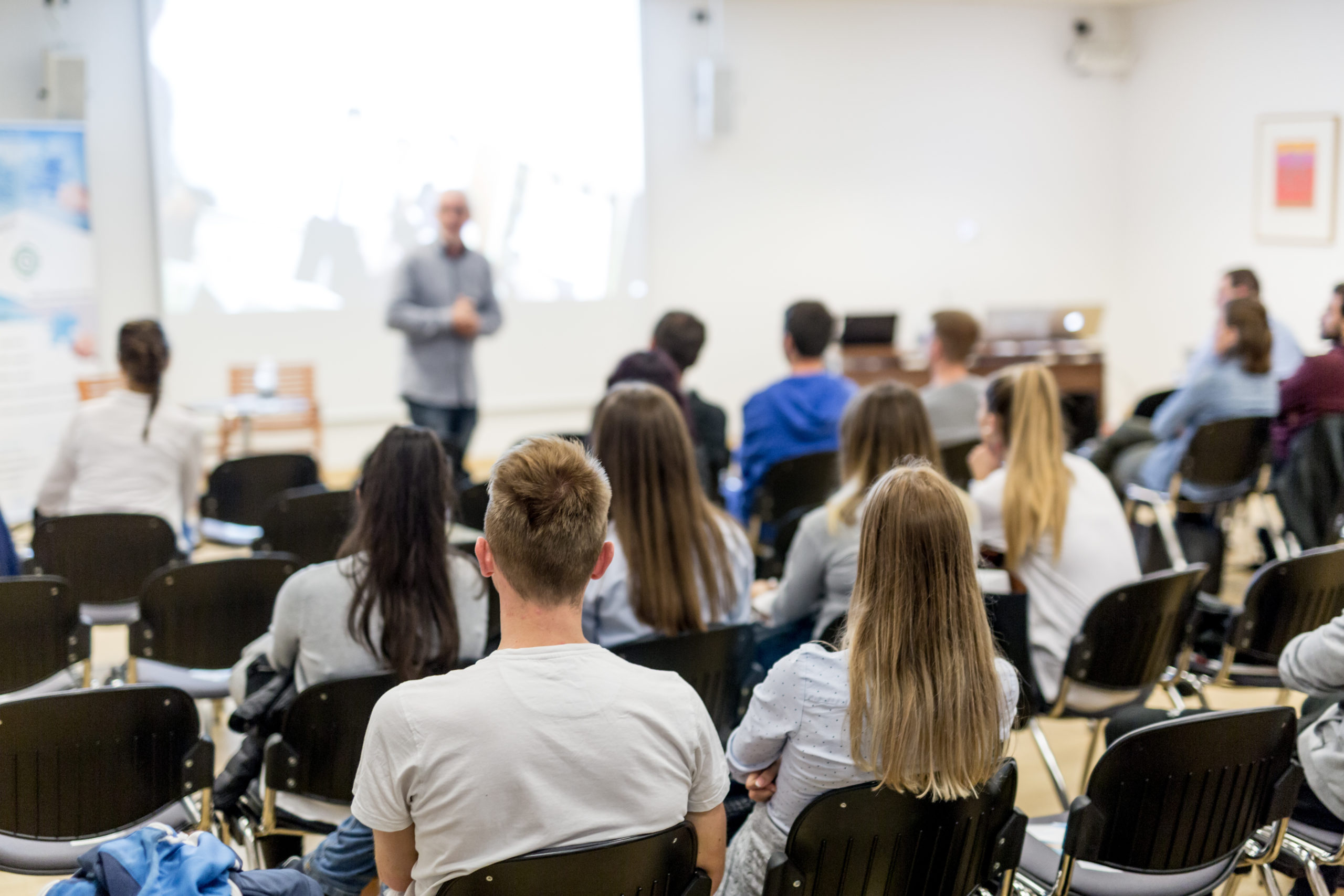 Speaker lecturing in lecture hall at university. Students listening to lecture and making notes.