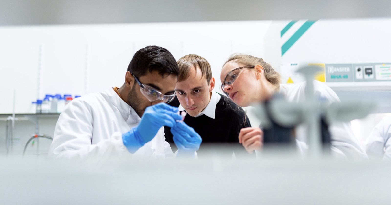 Three scientists examine vial