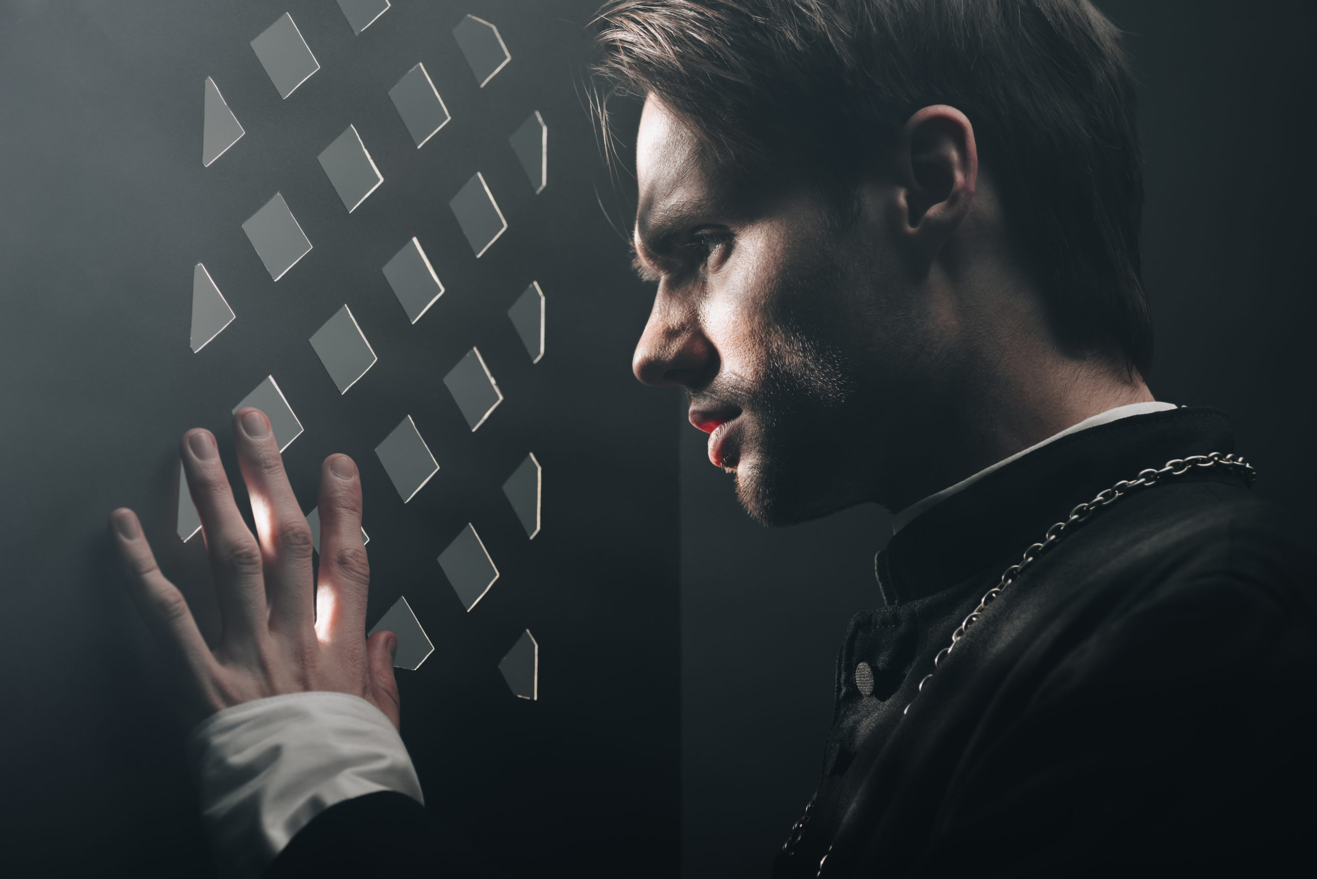 young tense catholic priest looking through confessional grille in dark with rays of light