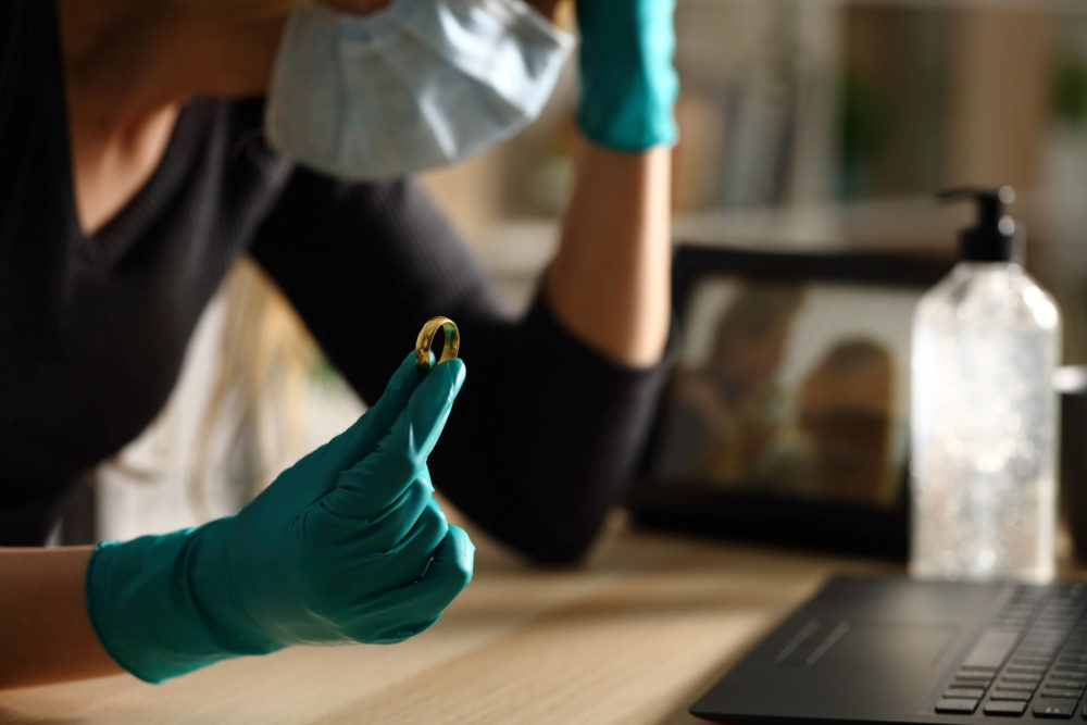 Close up of sad wife holding wedding ring after divorce on coronavirus confinement sitting on a desk at home in the night