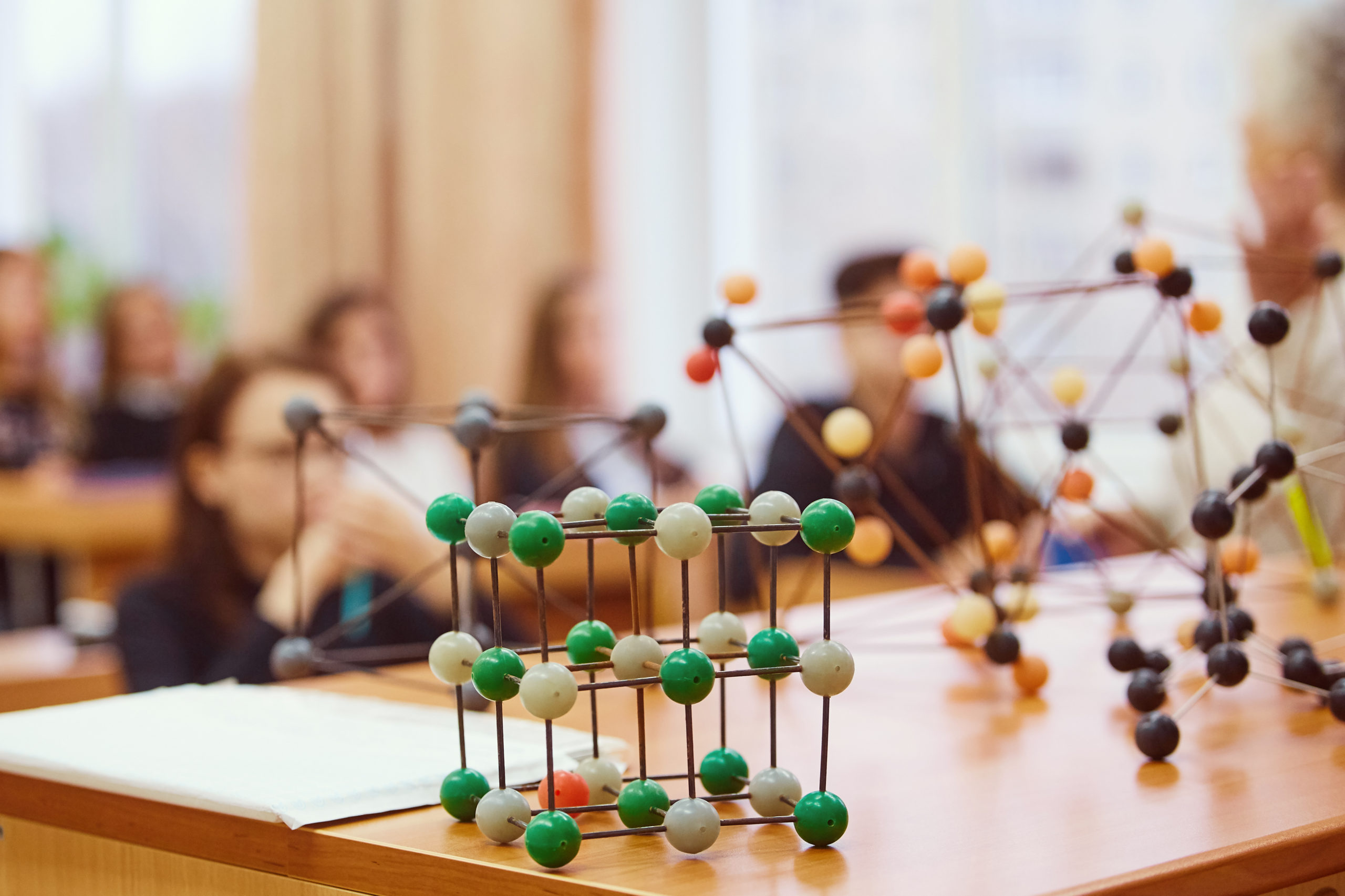 Students sit in the classroom and listen to a lecture in science. Plastic molecular educational model. Soft focus background image