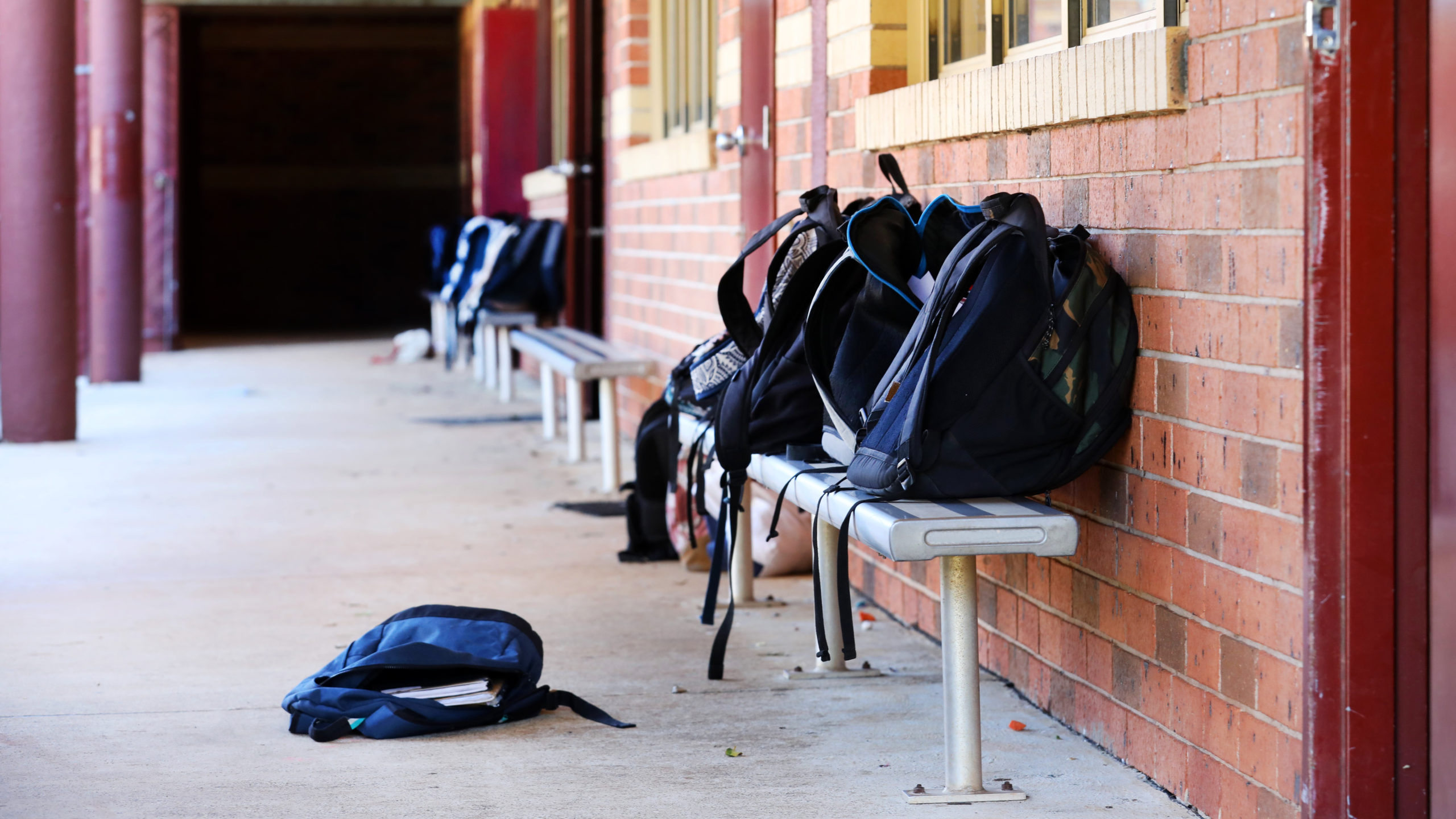 Authentic school grounds. School backpacks and bags piled up outside a run down looking classroom. Lesson learning taking place inside room.