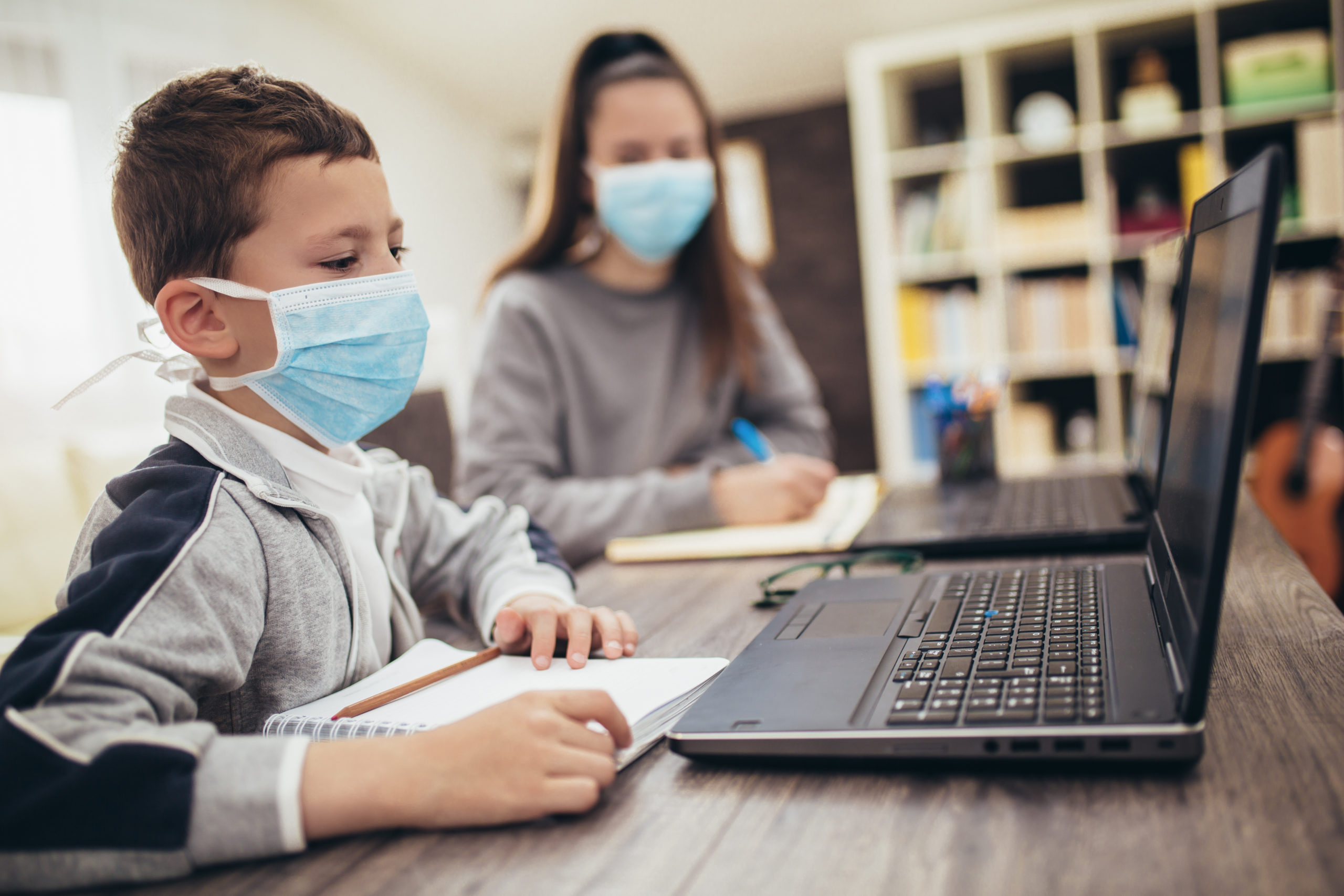 Boy and girl studies at home, wear protective masks, and doing school homework. Distance learning online education.