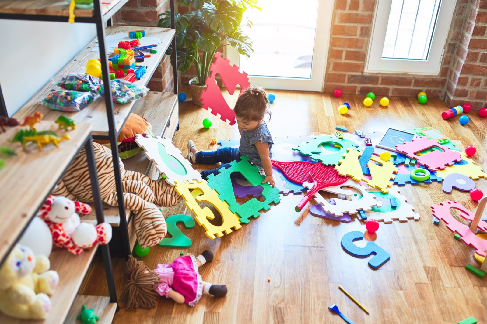 Beautiful toddler sitting on the floor playing with building blocks toy at kindergarten