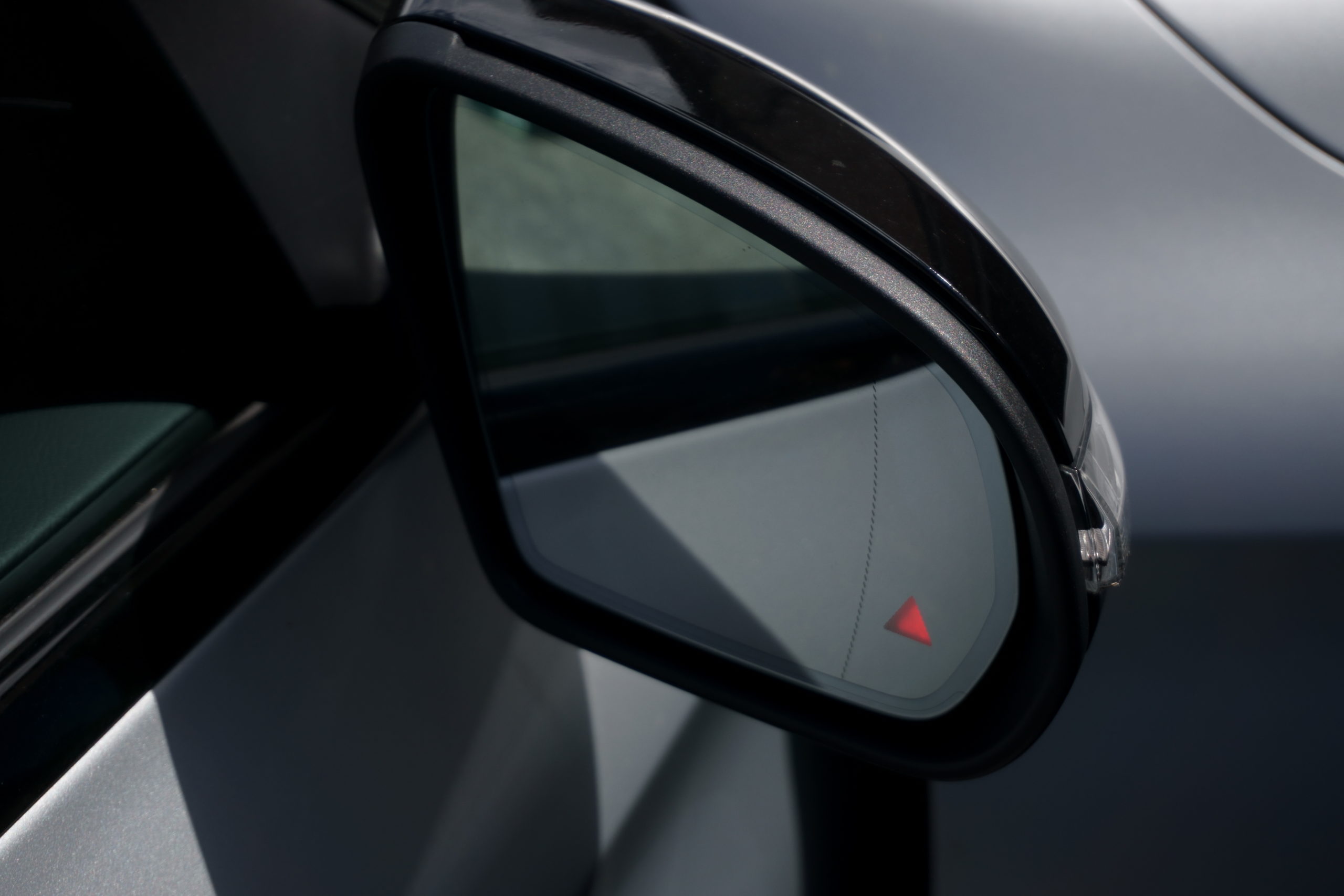 Car door mirror with illuminated blind spot monitoring light warning.