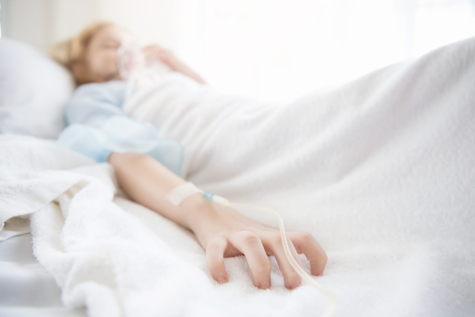 close up of saline on hand of sick girl lying on bed at hospital. Selective focus at finger.