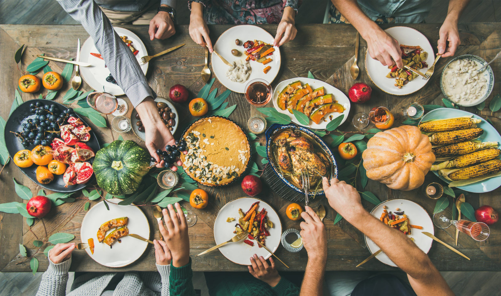 Thanksgiving, Friendsgiving holiday celebration. Flat-lay of friends feasting at Thanksgiving Day table with turkey, pumpkin pie, roasted vegetables, fruit, rose wine, top view