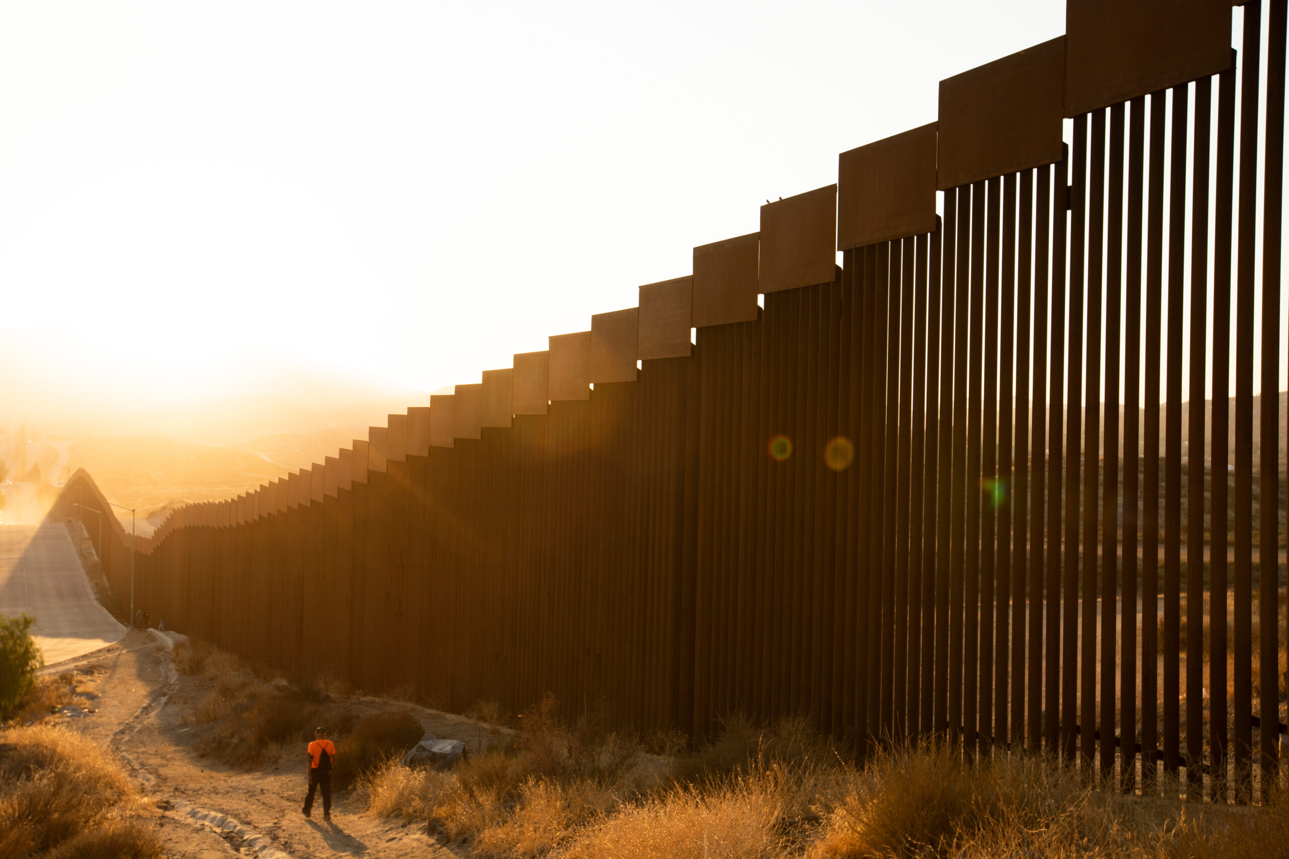 Tecate, Baja California, Mexico - September 14, 2021: Late afternoon sun shines on the USA Mexico border wall people walk in front of it.