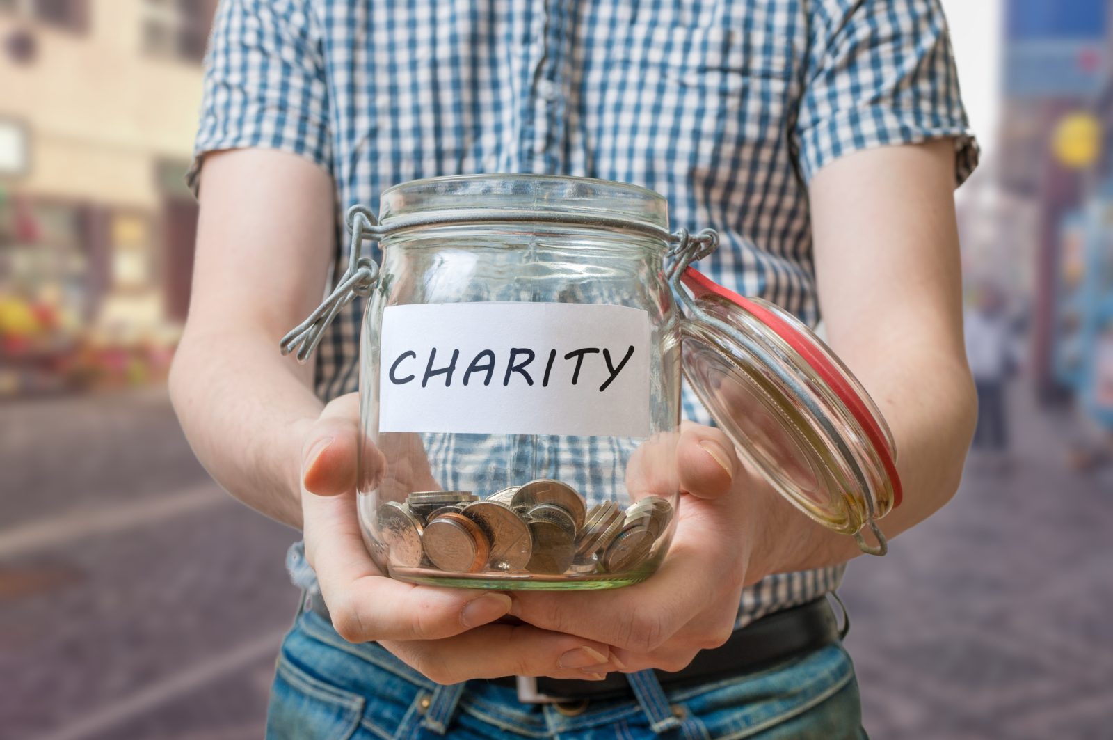 Man standing on street is collecting money for charity and holds jar with coins.