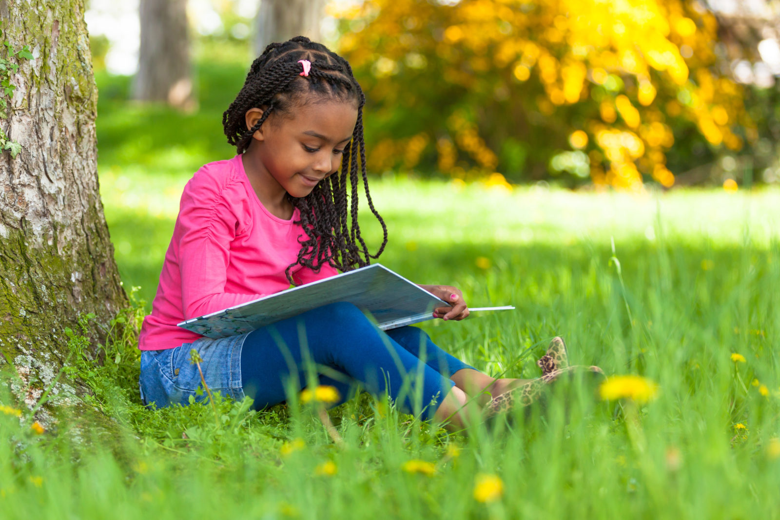 Outdoor portrait of a cute young black little girl reading a boo