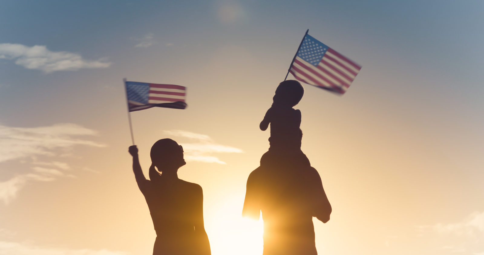 Patriotic man, woman, and child waving American flags in the air.