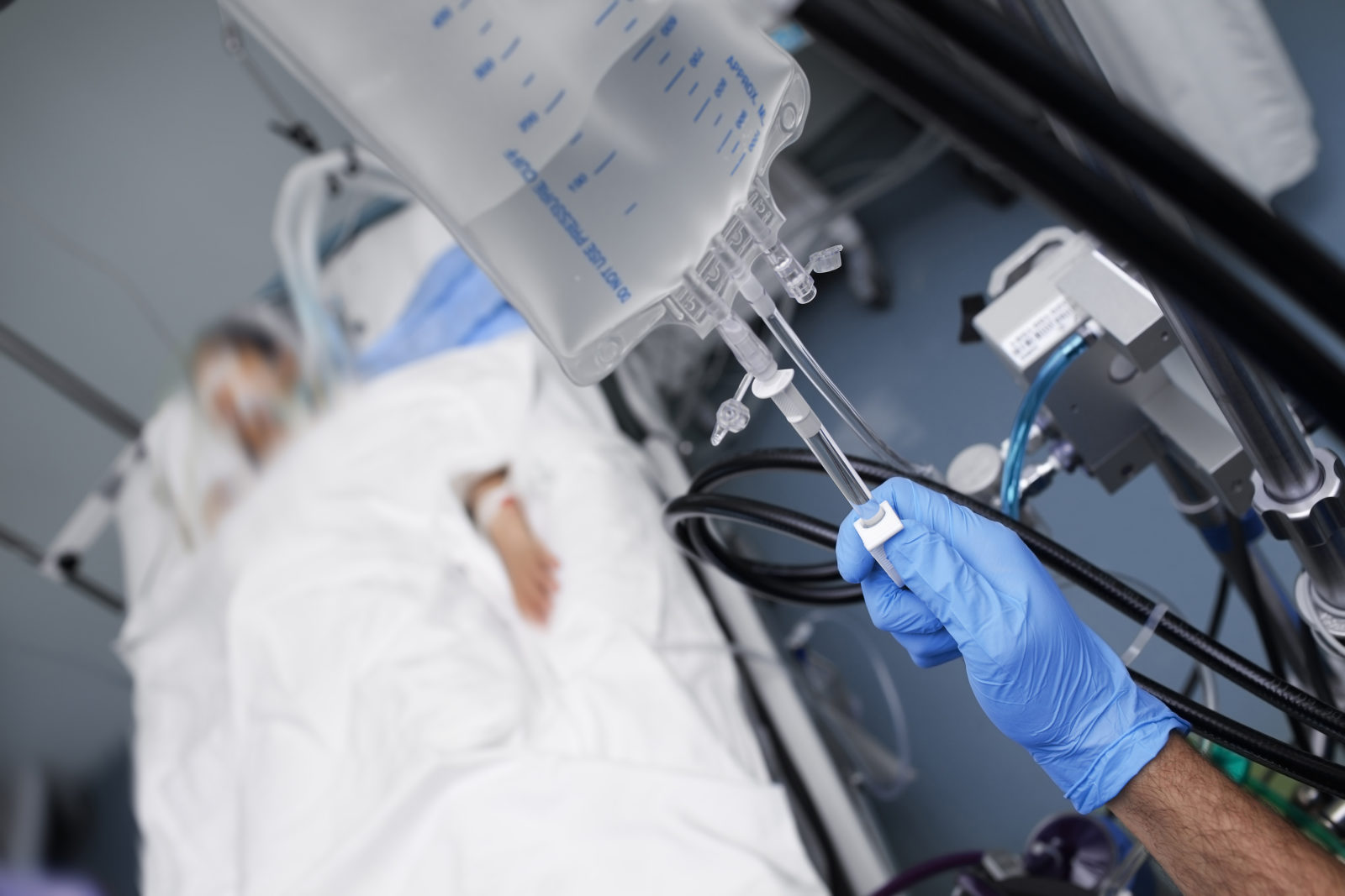 Male person with gloved hand turns off the intravenous drug system to the unconscious patient