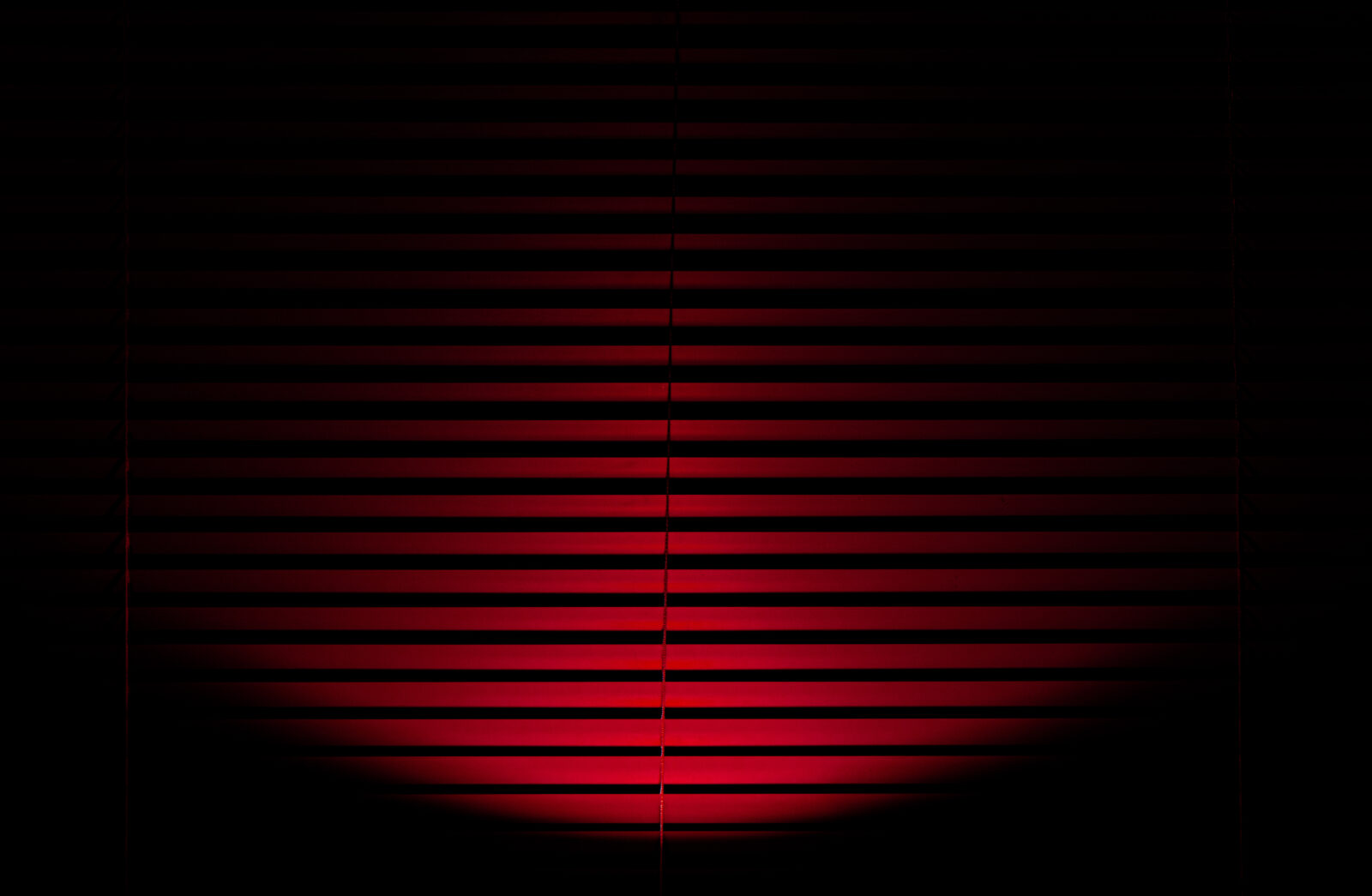 Red light shining onto closed red blinds creating a pattern of red and black lines in a semicircle