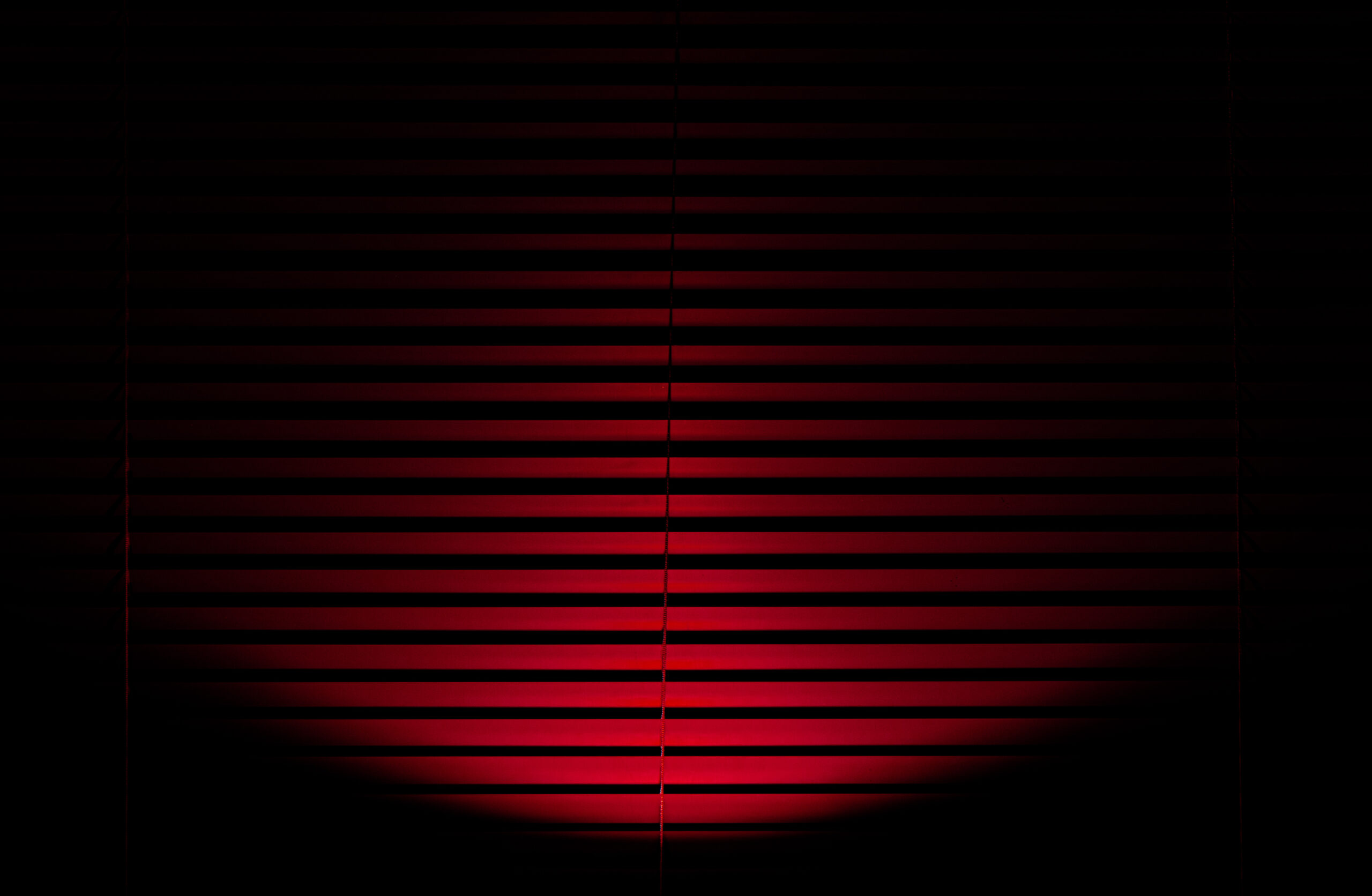 Red light shining onto closed red blinds creating a pattern of red and black lines in a semicircle