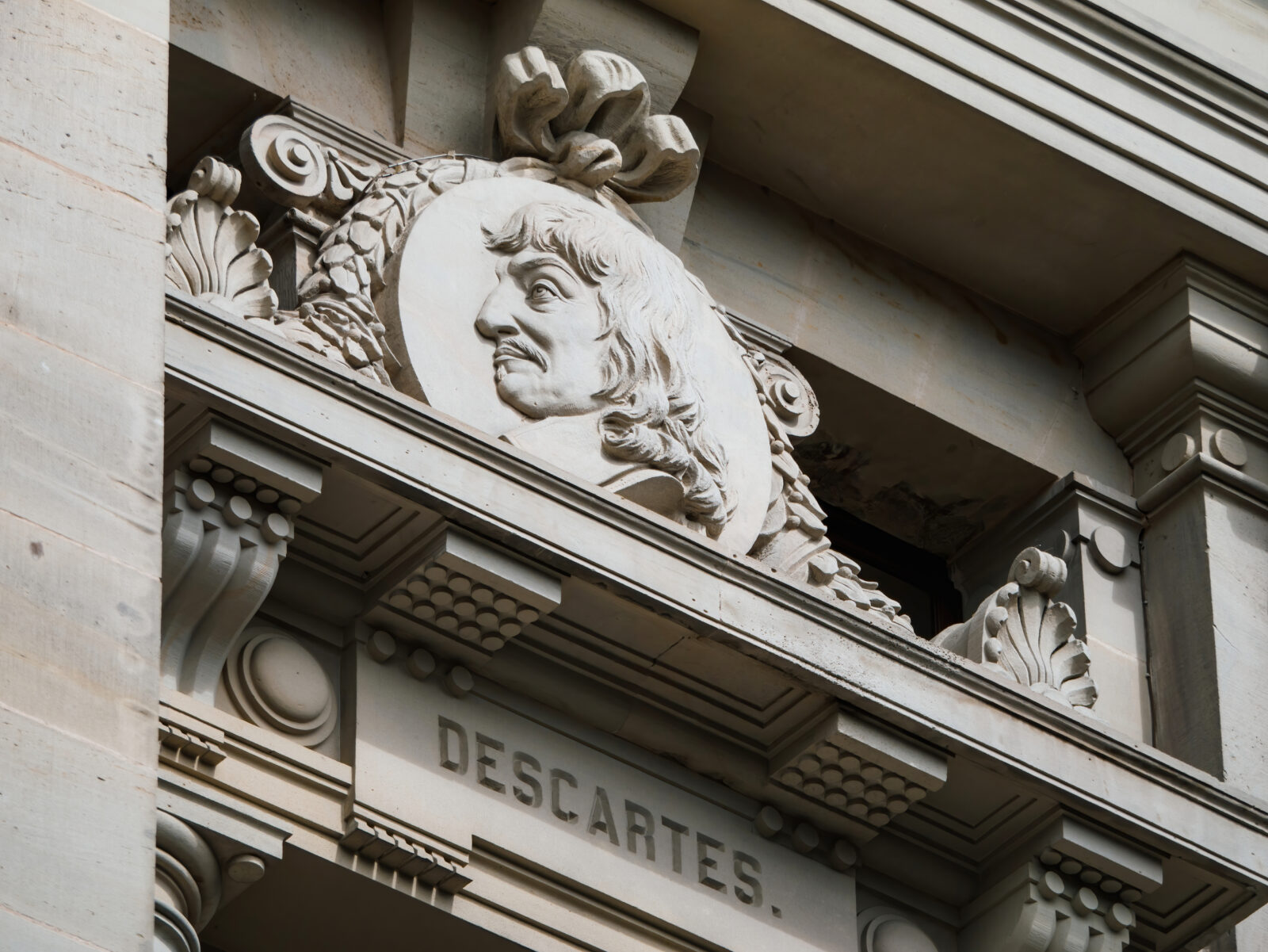 A low angle view of a statue of Rene Descartes against the historic building exterior, showcasing its intricate architecture and craftsmanship.