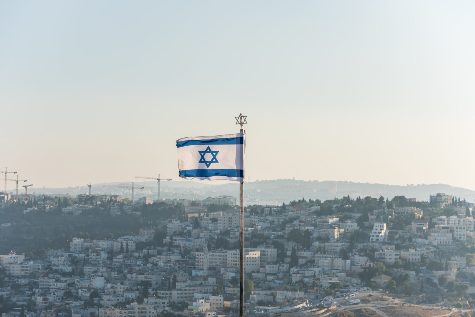 Israeli National flag waving on the top of Mount of Olive with background of residential houses in Jerusalem, Israel