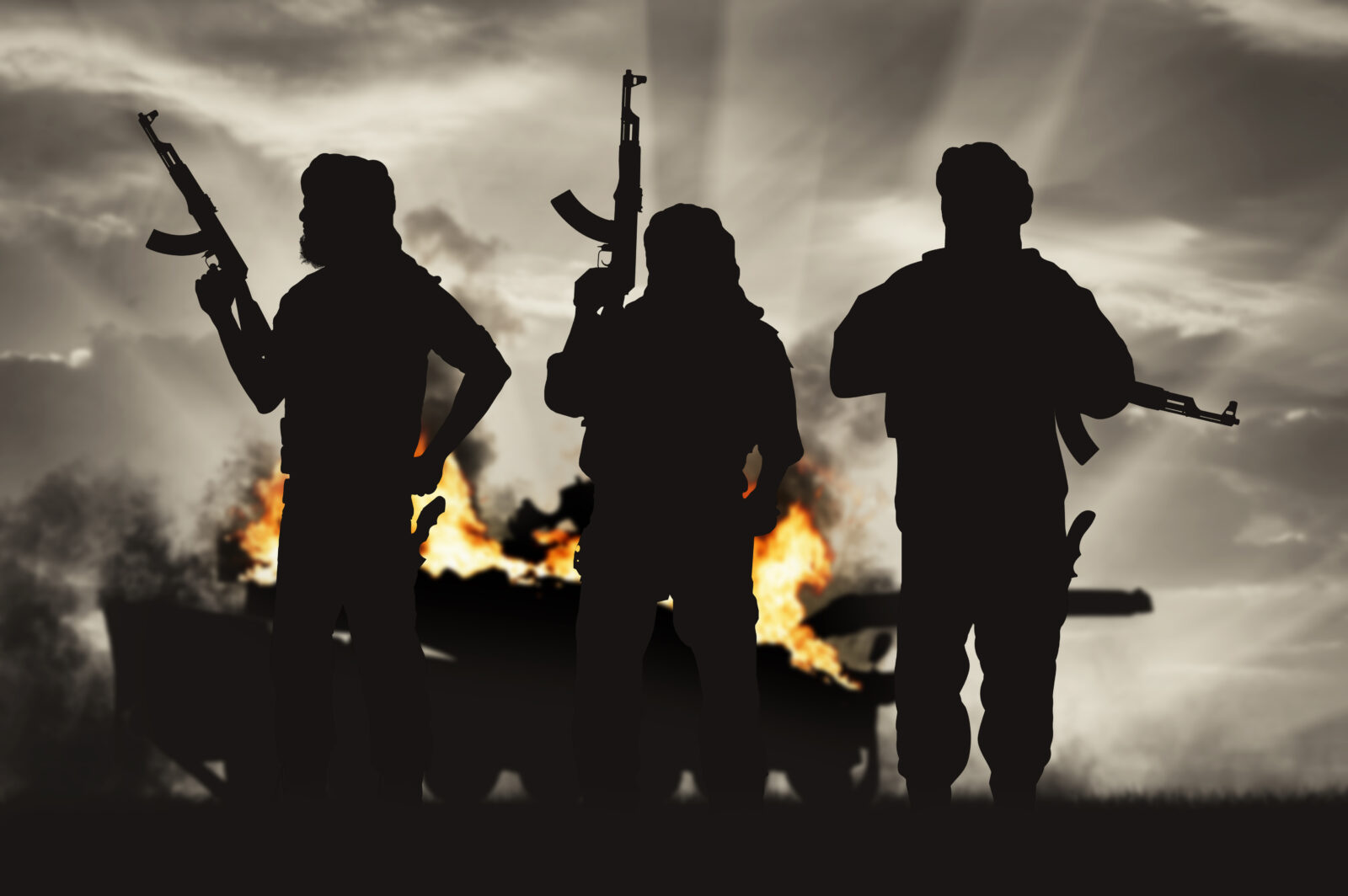 Silhouette of terrorist holding rifle against burning tank
