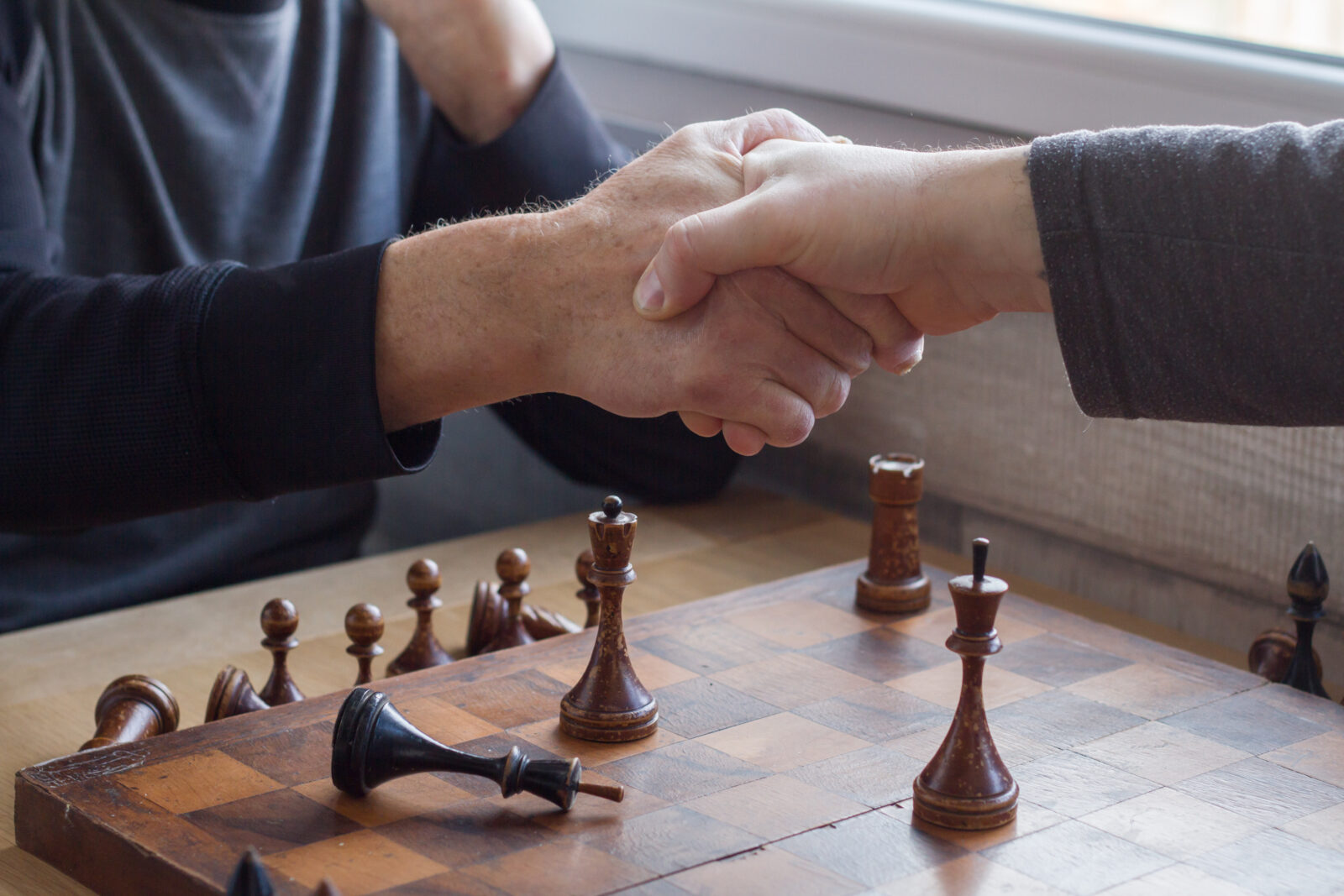 An old man shakes hands with an opponent in a game of chess, he lost and acknowledges it.