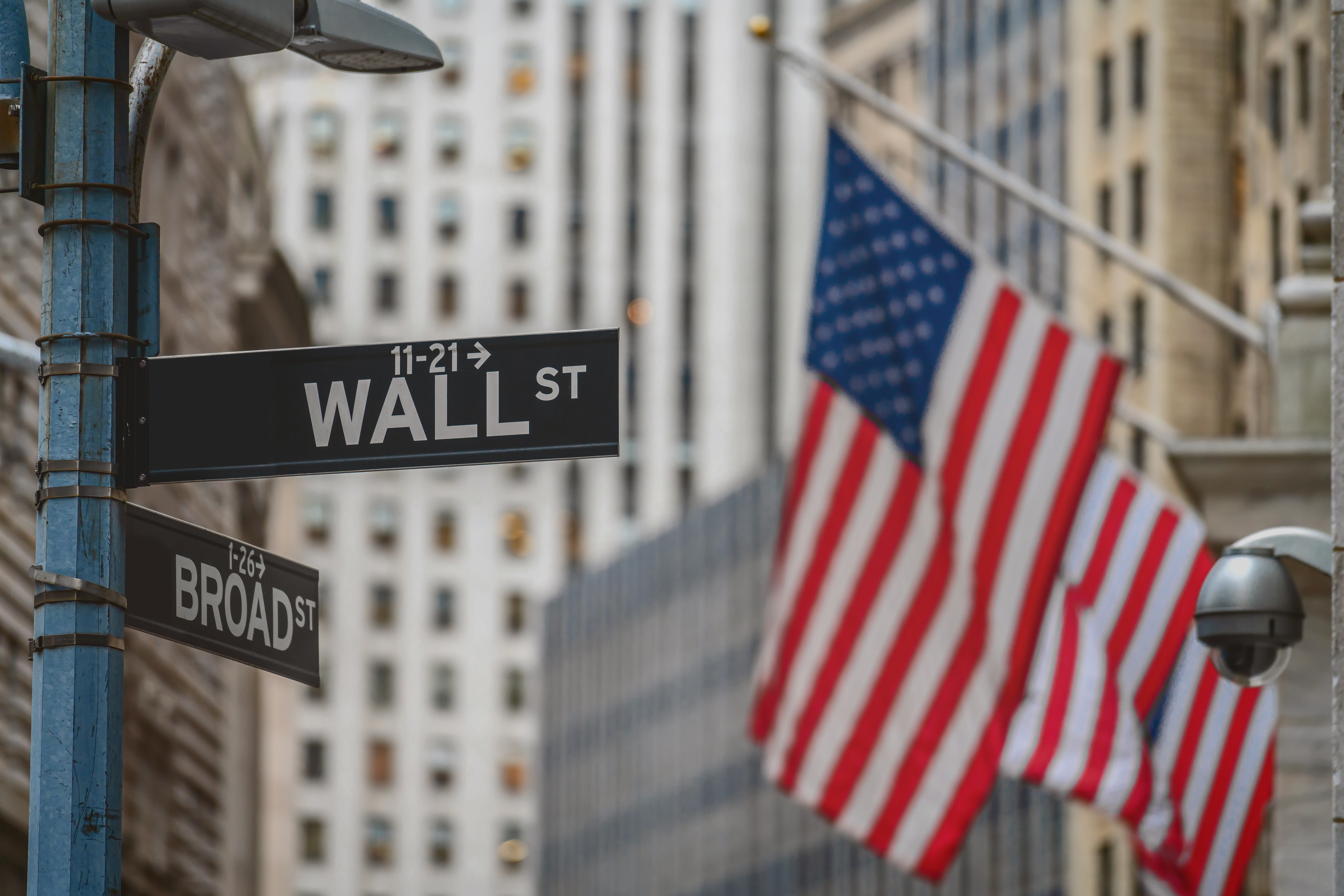 Wall Street "WALL ST" sign and broadway street over American national flags in front of NYSE stock market exchange building background. The New York Stock Exchange locate in economy district