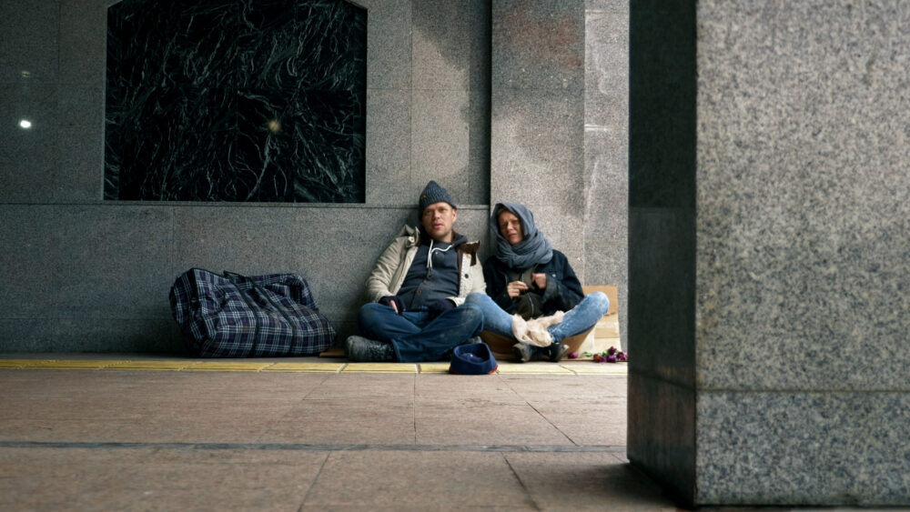 homeless people ask for alms sitting on the sidewalk against the wall