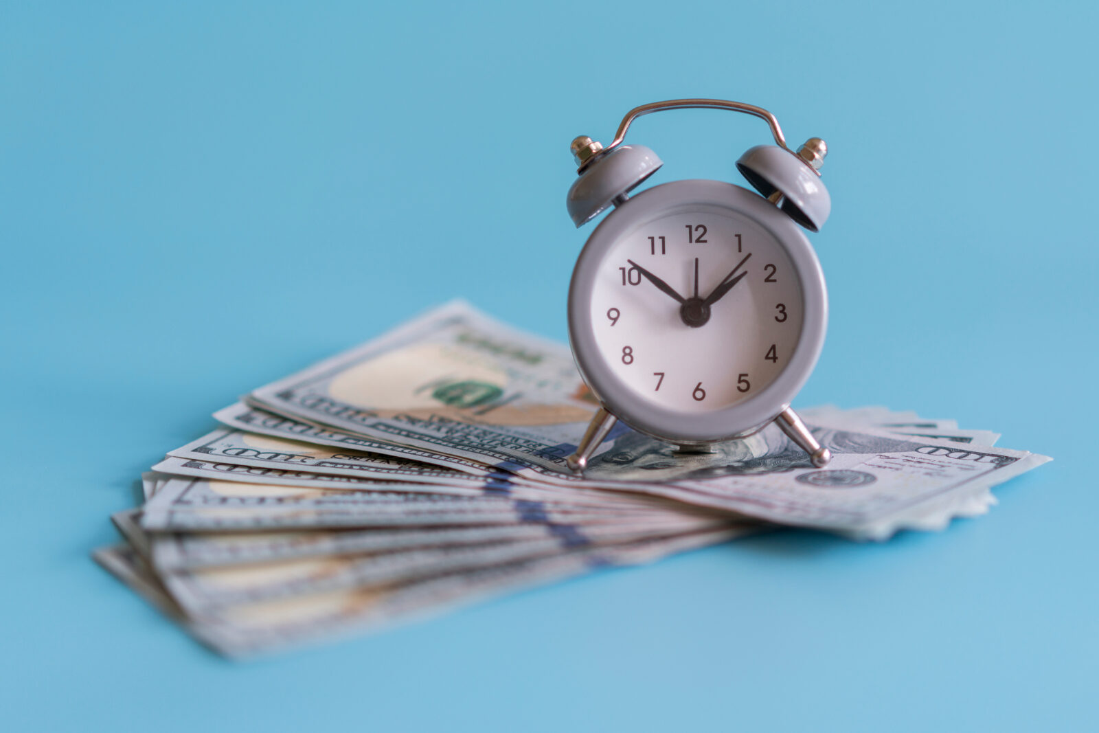 Alarm clock and dollars, close up. Time is money. Gray alarm clock on money banknotes Dollars, concept of business planning and finance. Finance concept with alarm clock and money in jar