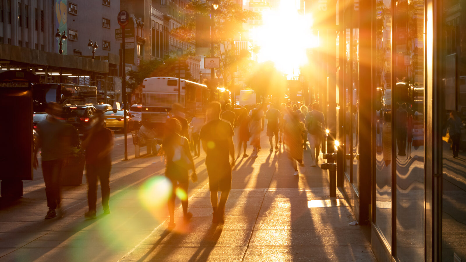 Sunlight shines on the diverse crowds of people walking down the busy sidewalk on 34th Street through Midtown Manhattan in New York City