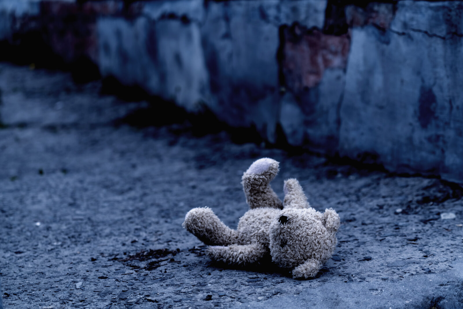 Dirty teddy bear toy lies outdoors on the road as symbol of children's loneliness, pain, loss childhood and future. Copy space for text or design.