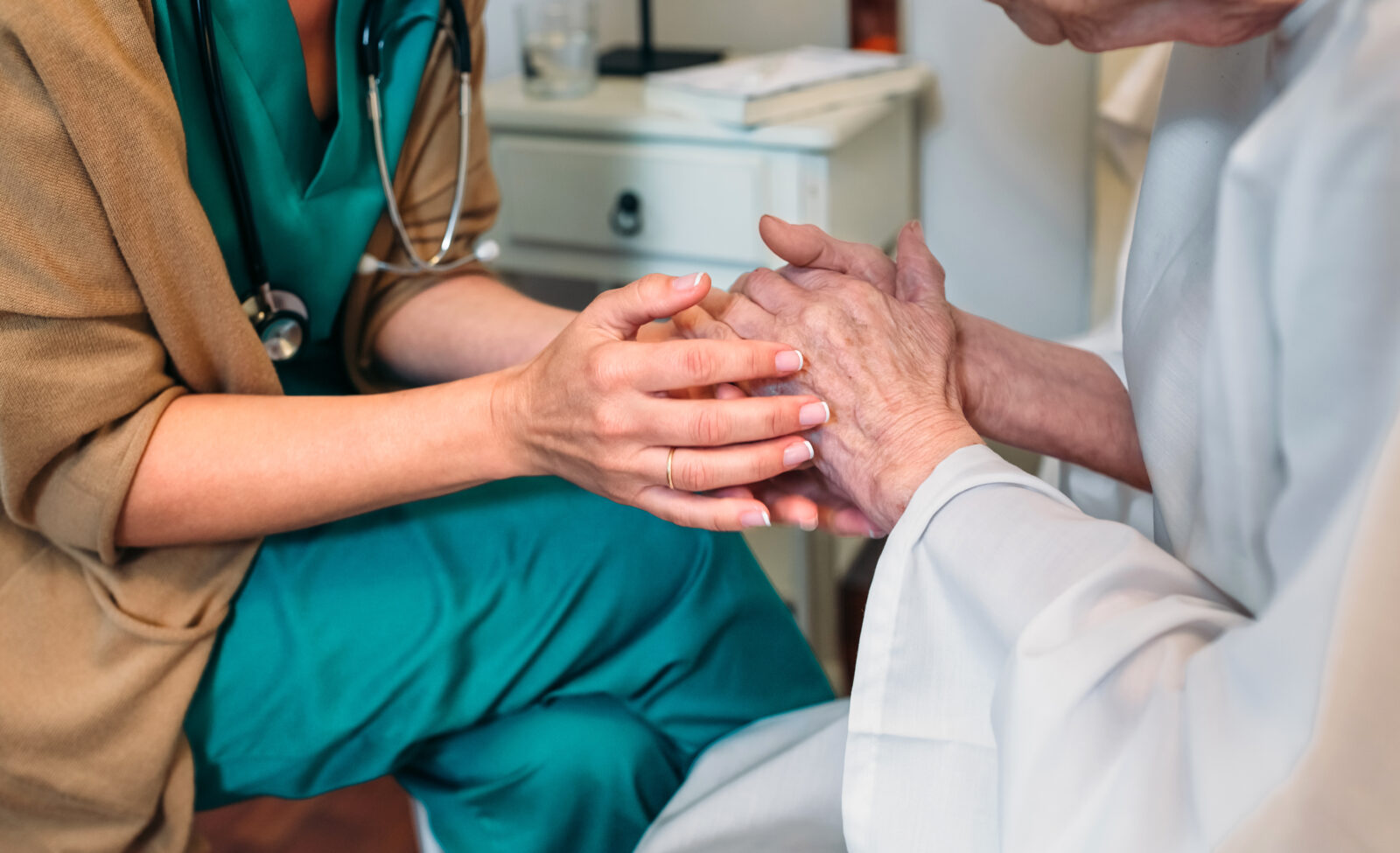 Female doctor giving encouragement to elderly patient by holding her hands