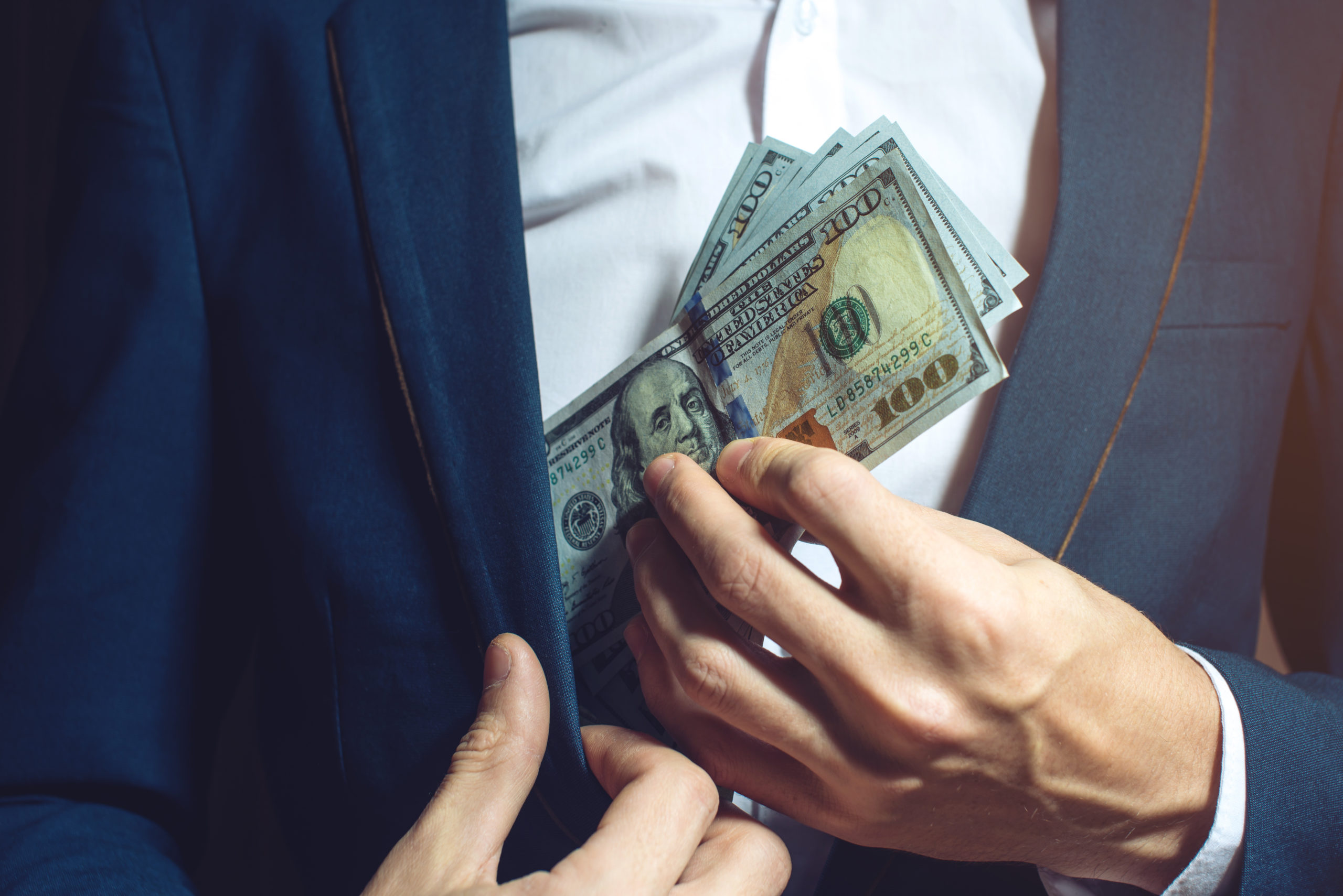 man businessman in suit taking notes, bills of dollars in his pocket as a bribe. the concept of corruption and bribery