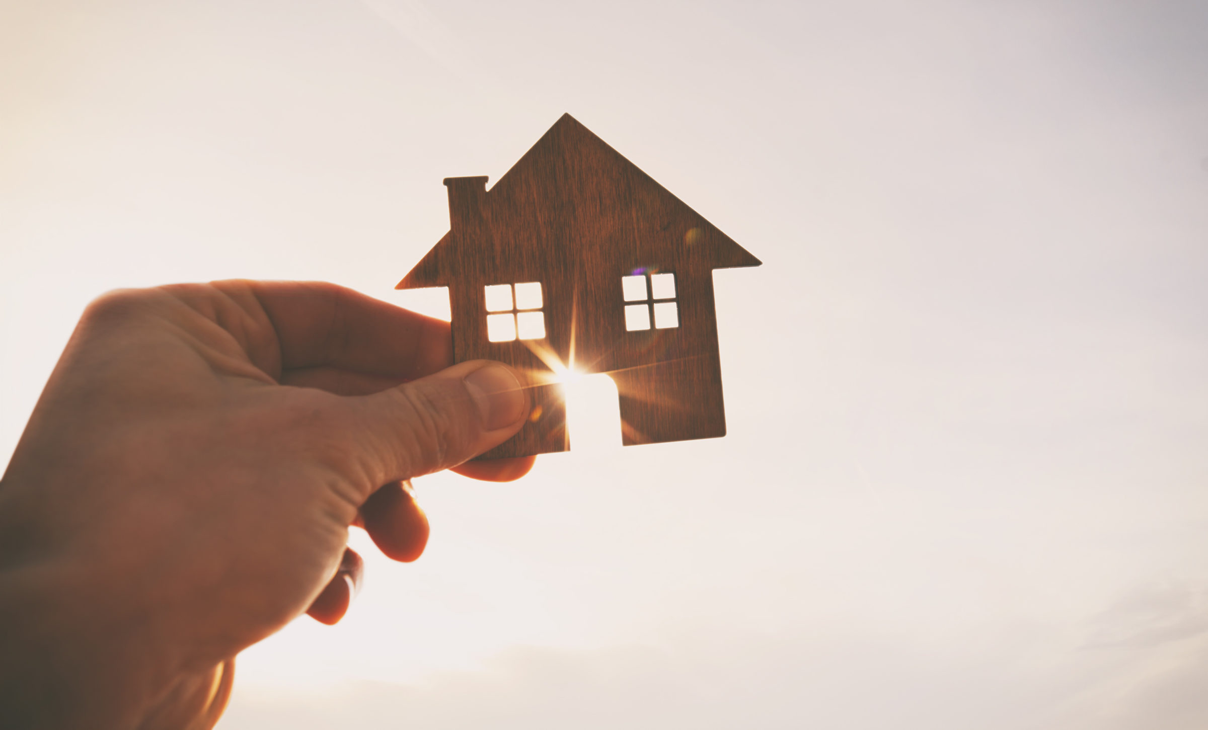 Man's hand holds wooden flat house against the sun