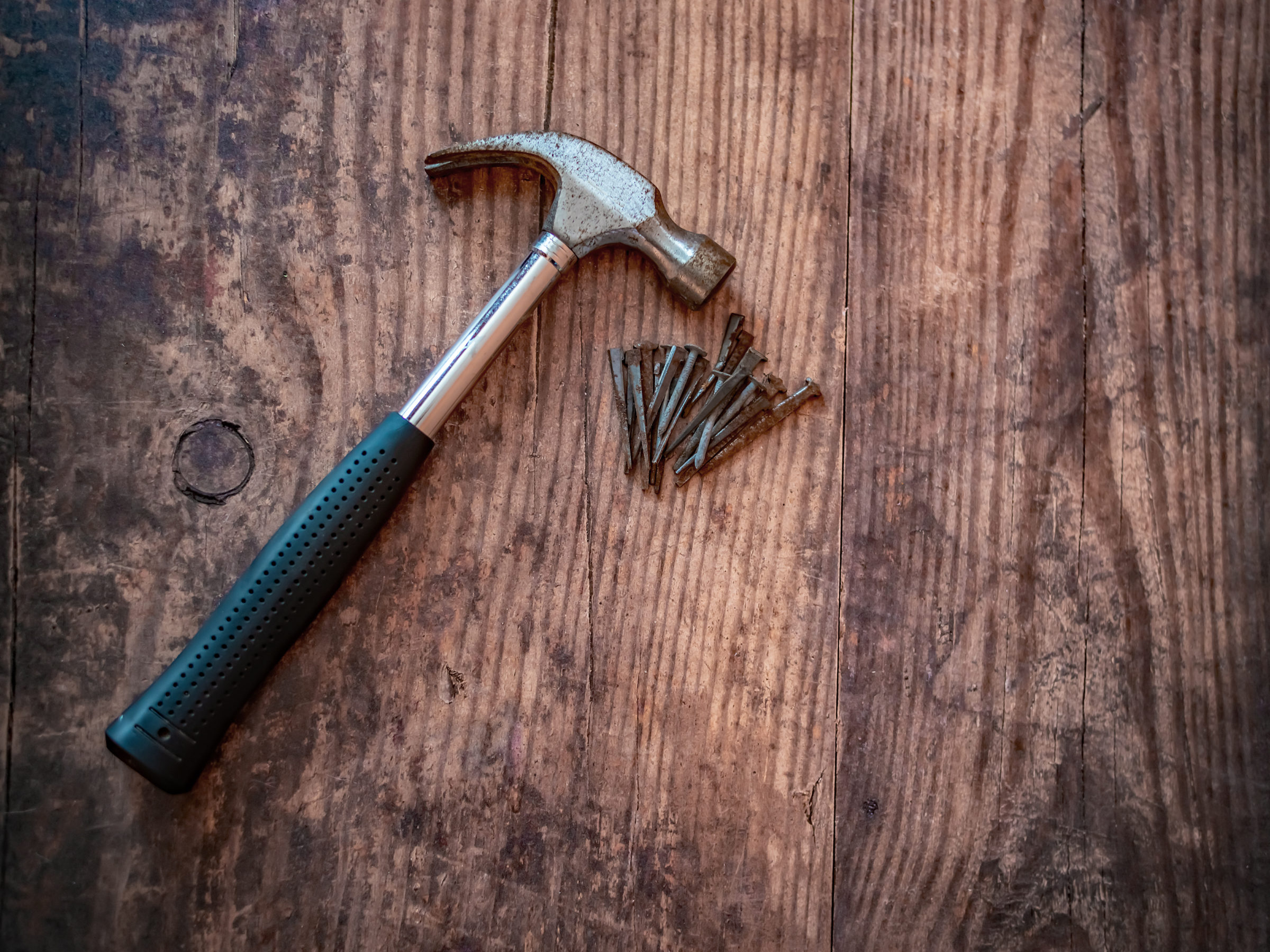 Top down view of claw hammer and rusty nails on a plain wooden background