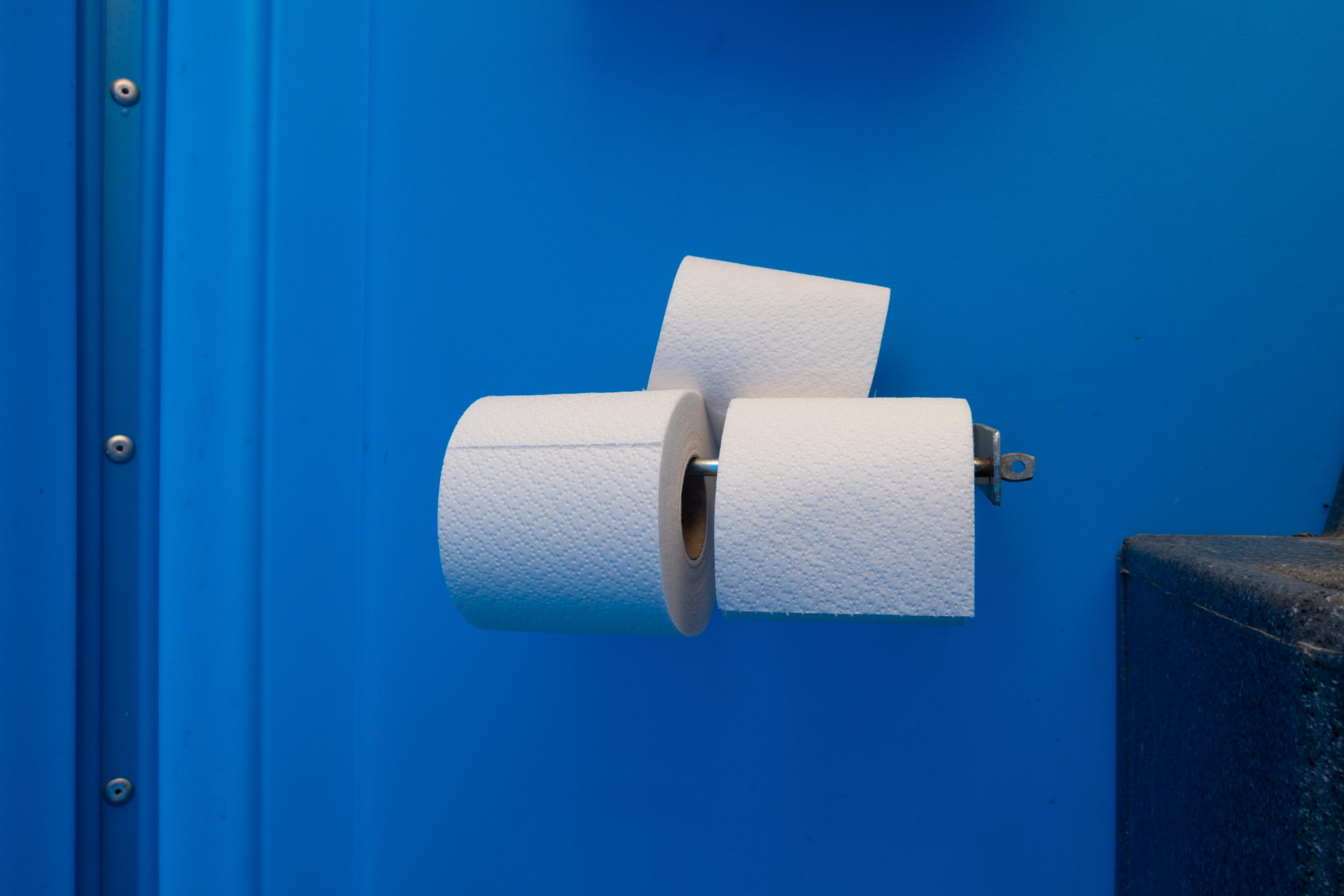3 toilet paper rolls are located on a blue wall of a mobile toilet
