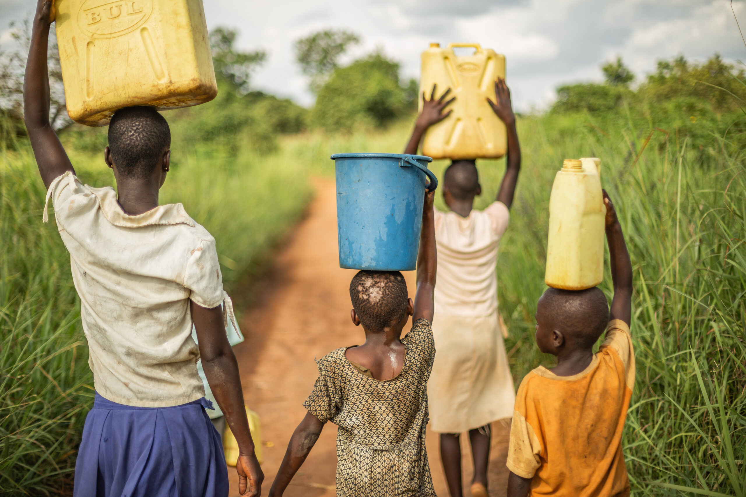 Group of young African kids walking with buckets and jerrycans on their head as they prepare to bring clean water back to their village.