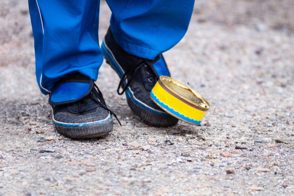 Old used can of street football game. Legs of a young man in sneakers. Children's street games with a can on the road.