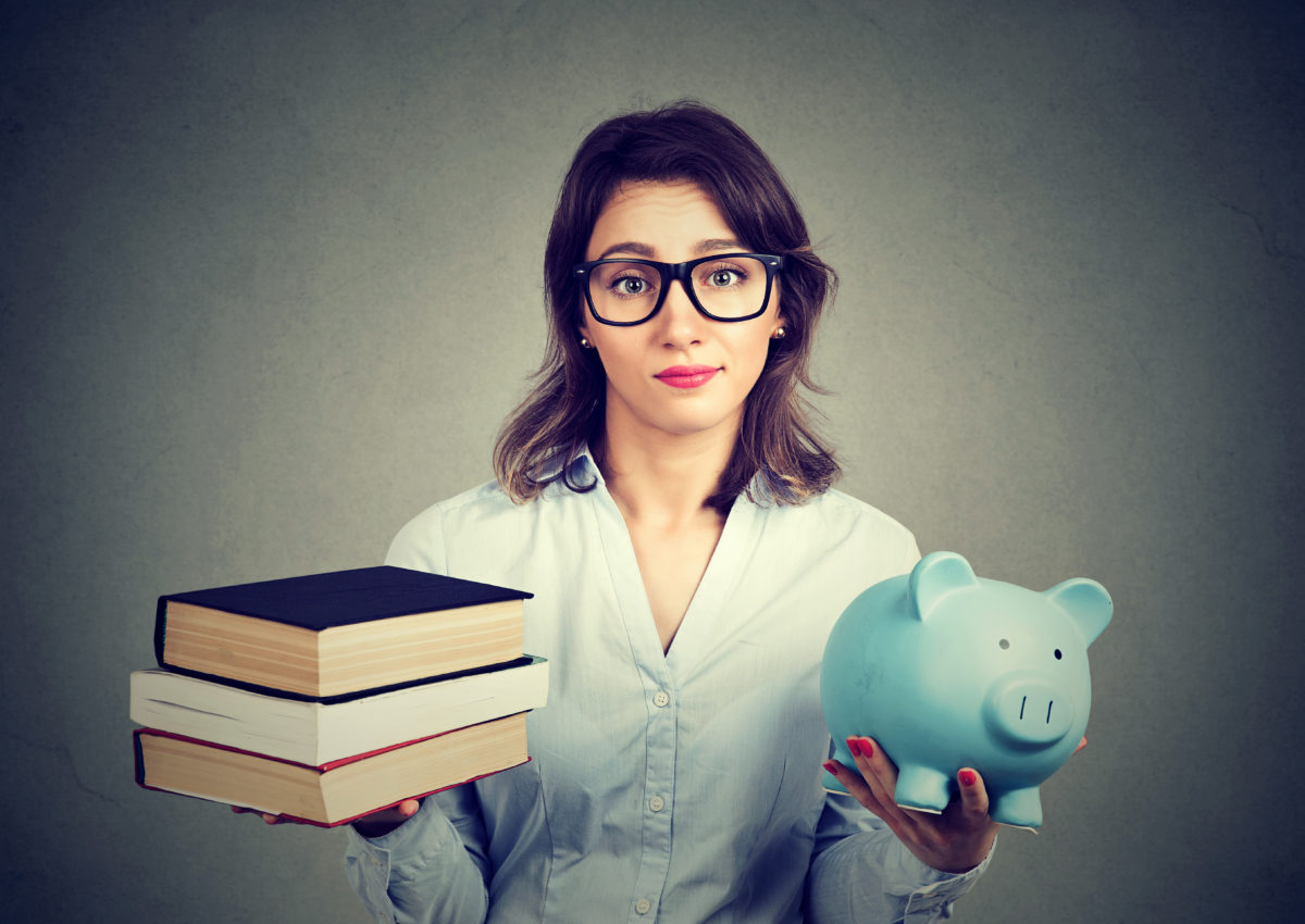 Student loan concept. Young woman with stack pile of books and piggy bank full of debt rethinking future career path