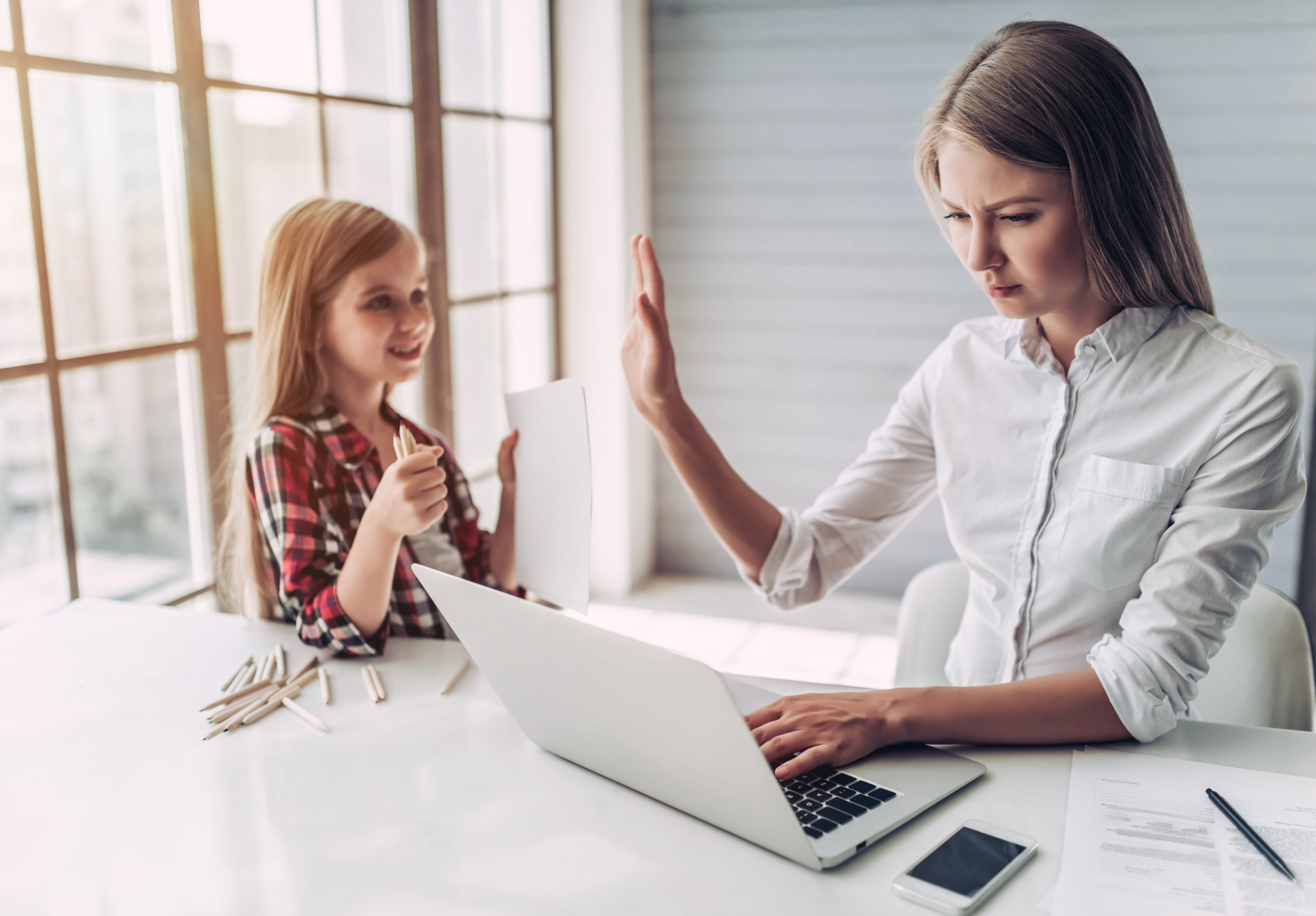 I'm busy! Beautiful young woman is working at home with her little cute daughter nearby. Don't have enough time for child.