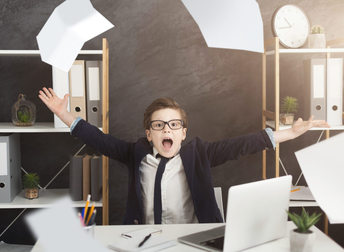 Bureaucracy, exhausting paperwork. Stressed little boy in suit throwing papers in air, sitting at office, copy space