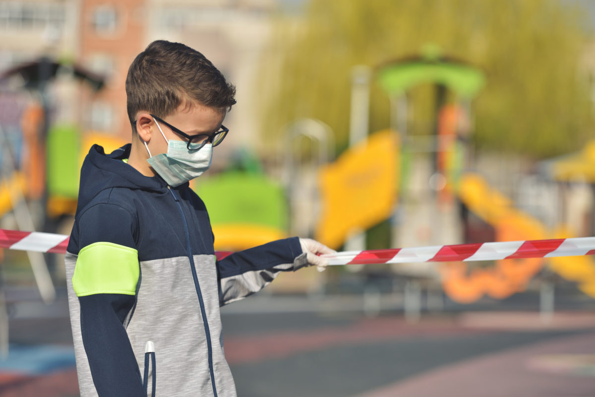 Disappointed lonely kid wearing mask for protection of corona virus spread on a closed empty park