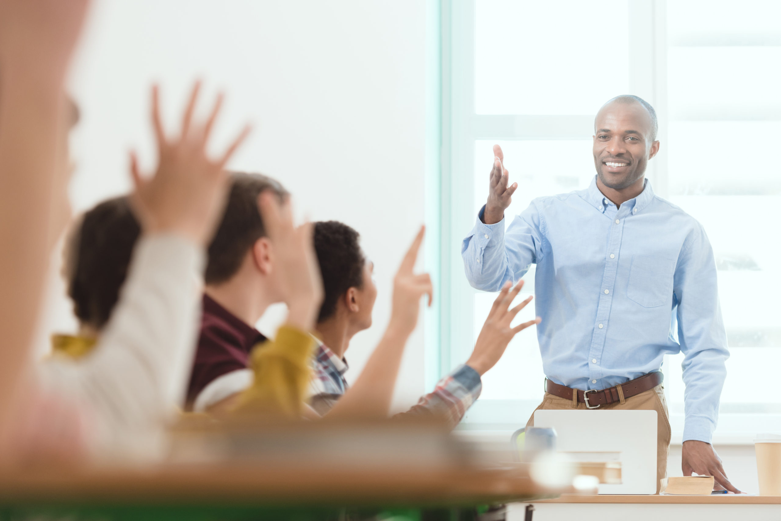 Smiling african american teacher and schoolchildren with arms up in classroom