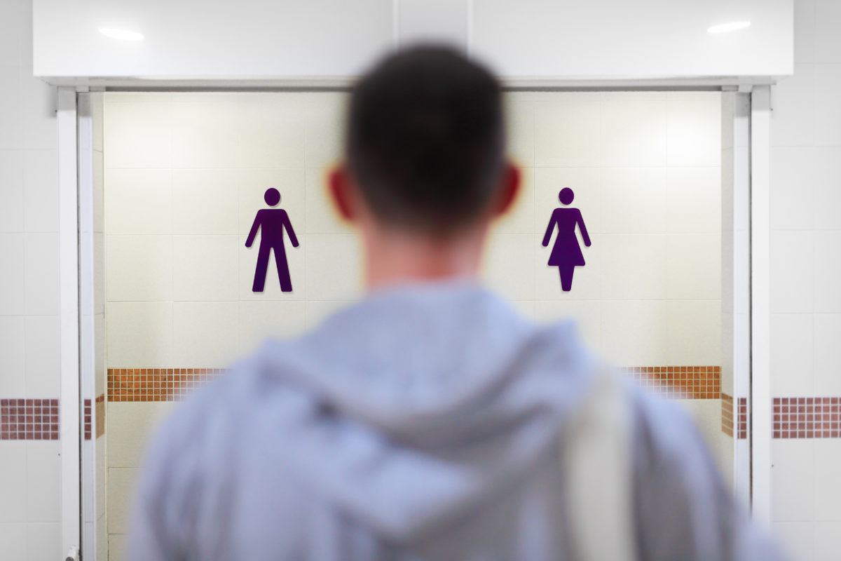 Transgender guy standing in front of man and woman toilet.