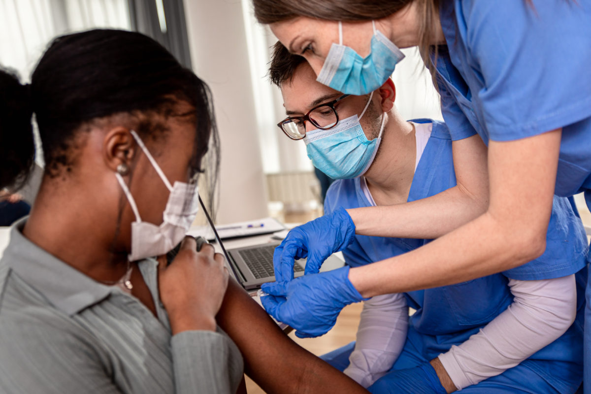 Female nurse with mask giving vaccine to patient in clinic.