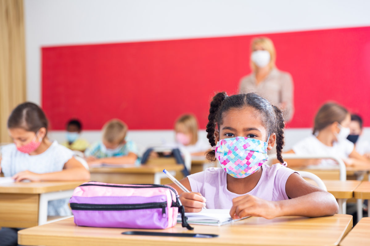 Portrait of focused schoolgirl wearing protective face mask working at lesson in classroom, writing exercise