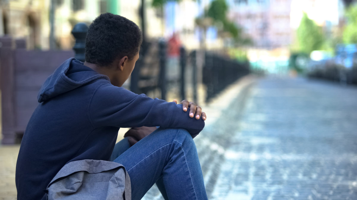 Sad mixed-race teenager sitting on sidewalk, relationship problems, awkward age