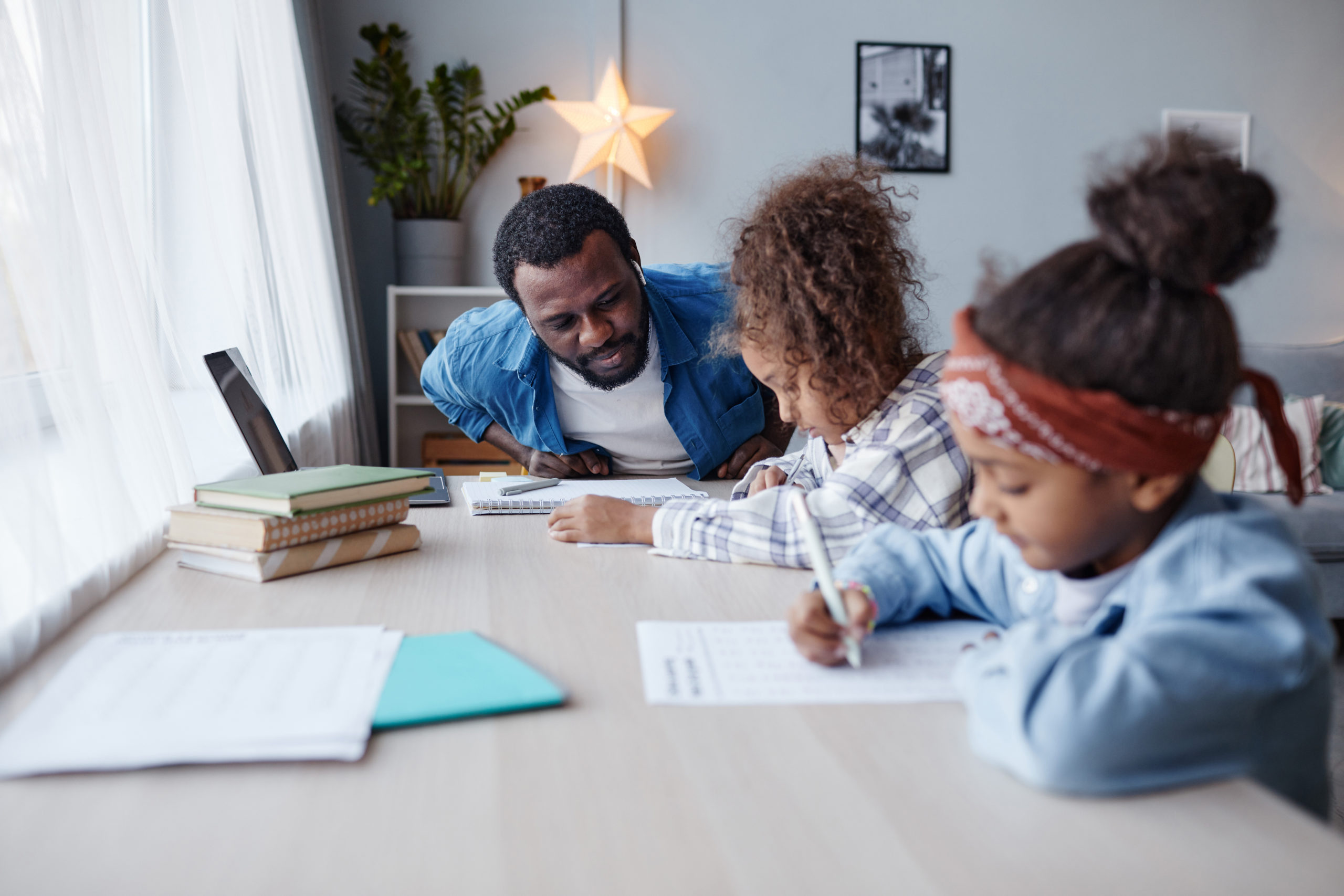 Portrait of caring father doing homework with two little girls at home, copy space