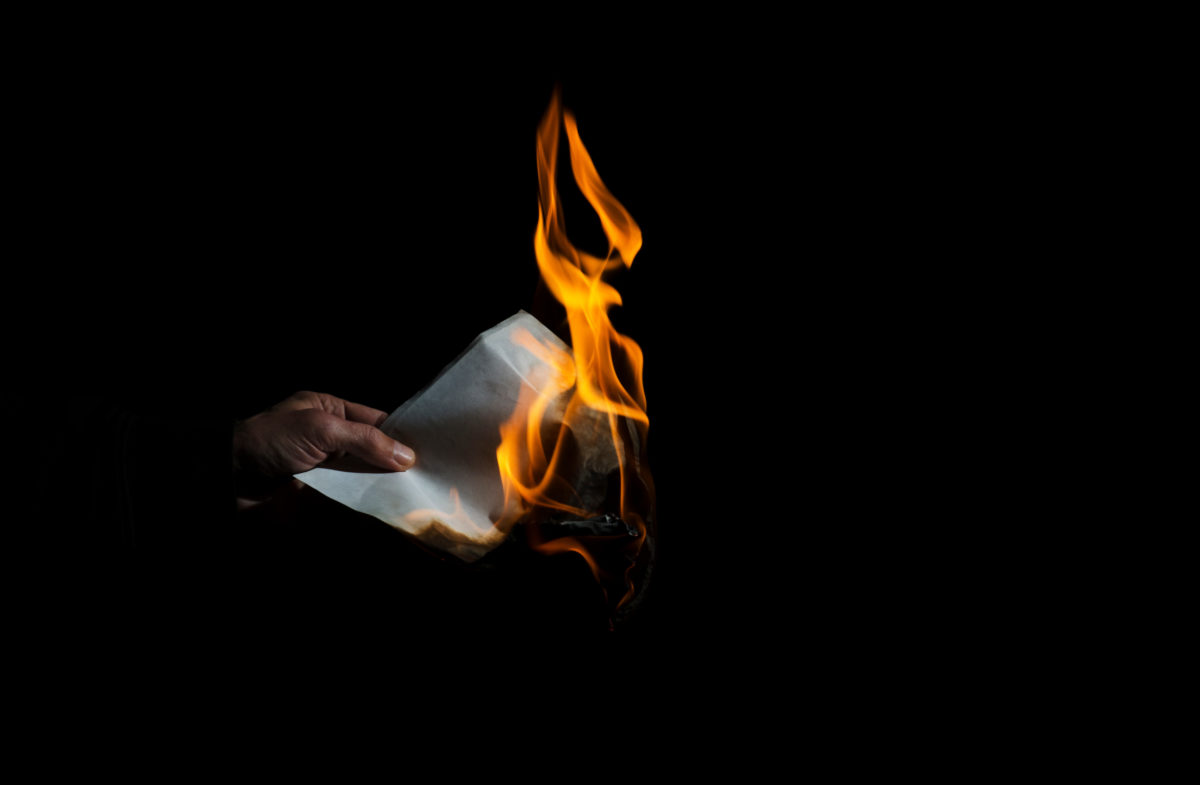 Burning sheet of paper in the male hand.