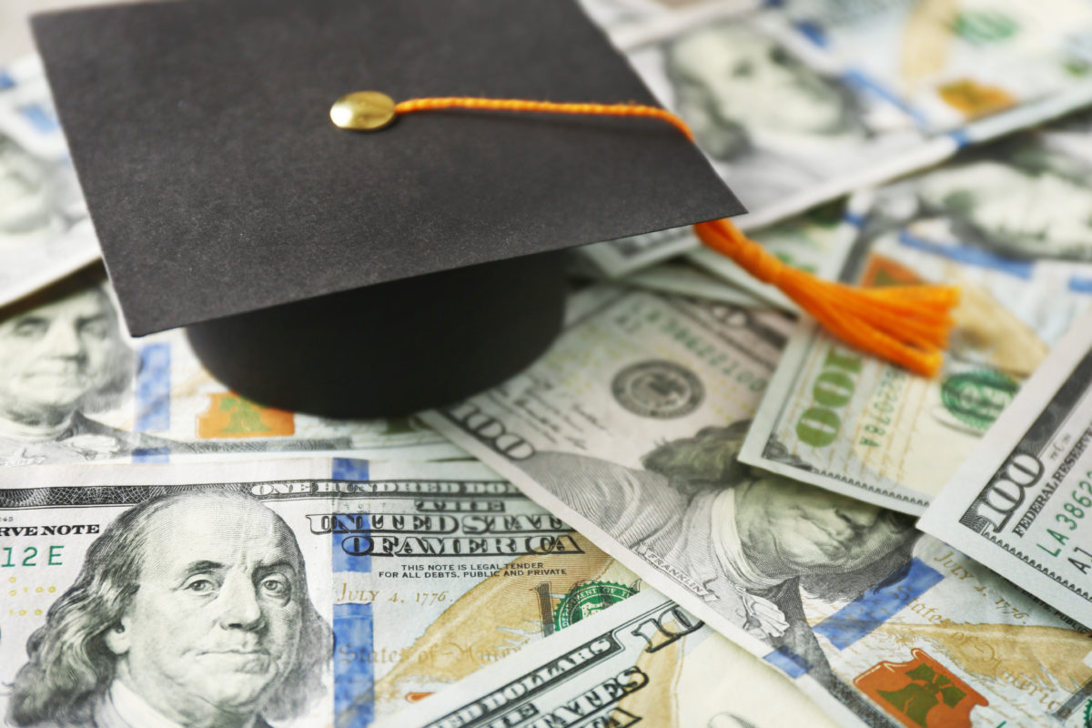 Close up view of graduation hat on dollar banknotes. Tuition fees concept