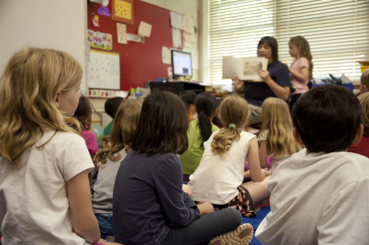 Captured in a metropolitan Atlanta, Georgia primary school, this photograph depicts a typical classroom scene, where an audience of school children were seated on the floor before a teacher at the front of the room, who was reading an illustrated storybook, during one of the scheduled classroom sessions. One of the female students was assisting the teacher, while the rest of the class listened attentively to the instructor’s narrative.